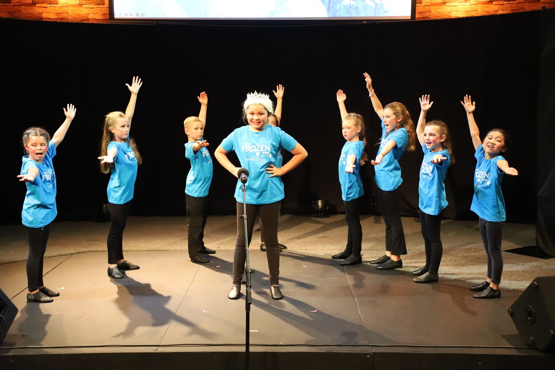 A group of children are singing into a microphone on a stage.