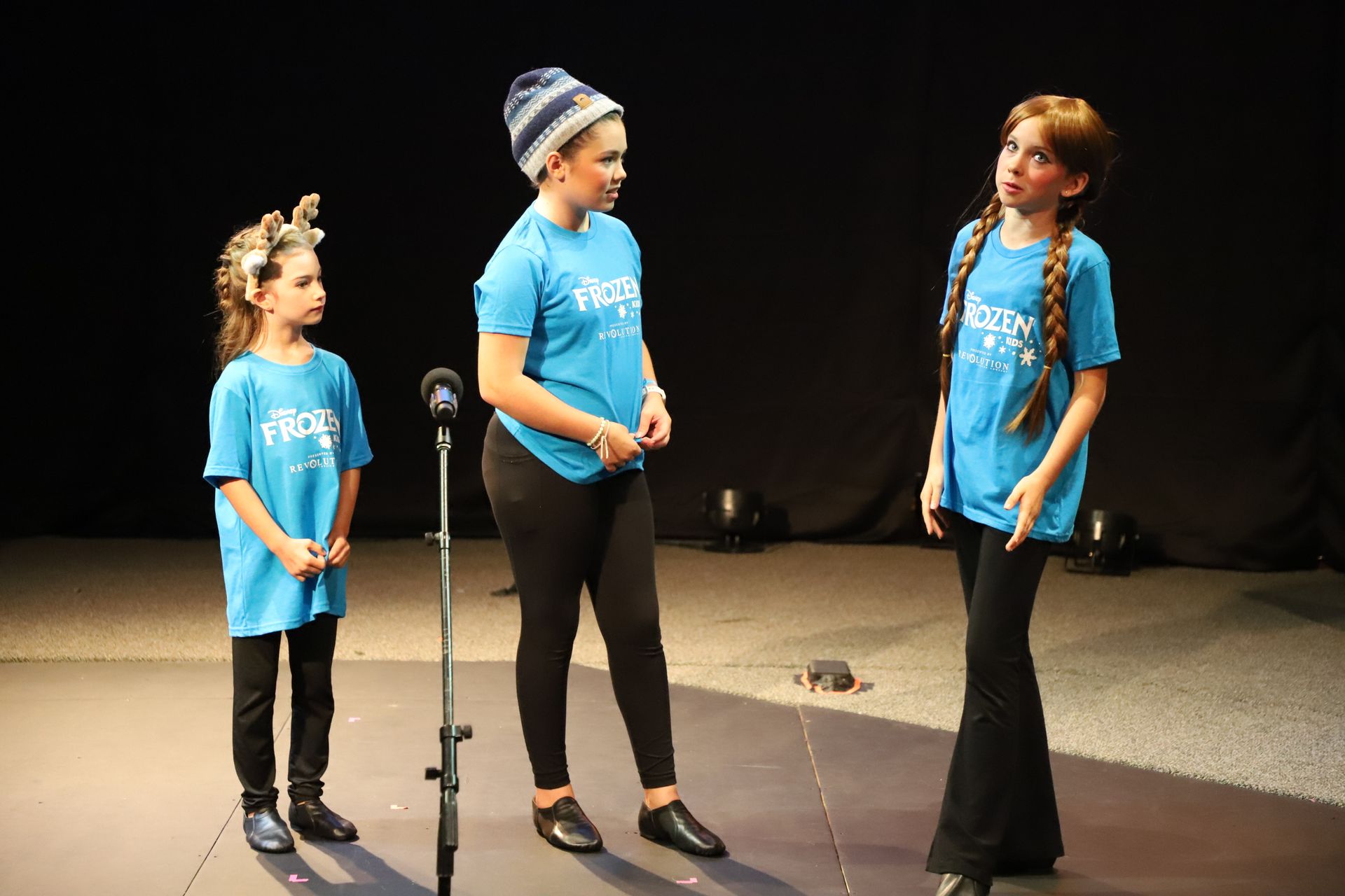 Three young girls are standing in front of a microphone on a stage.