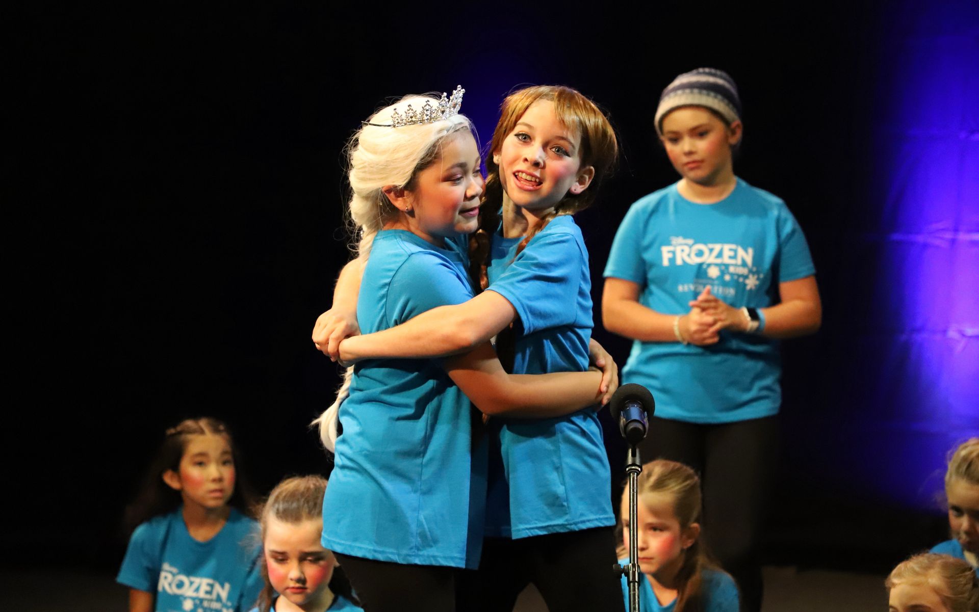 A group of young girls are hugging each other on a stage.
