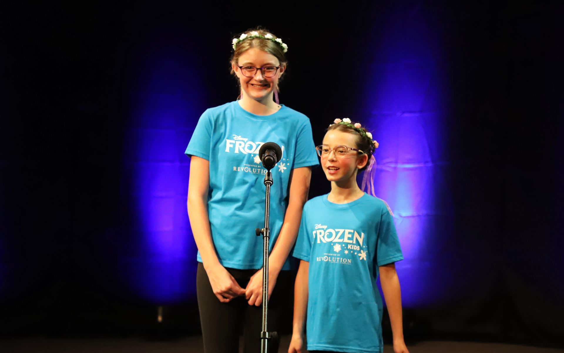 Two young girls are singing into microphones on a stage.