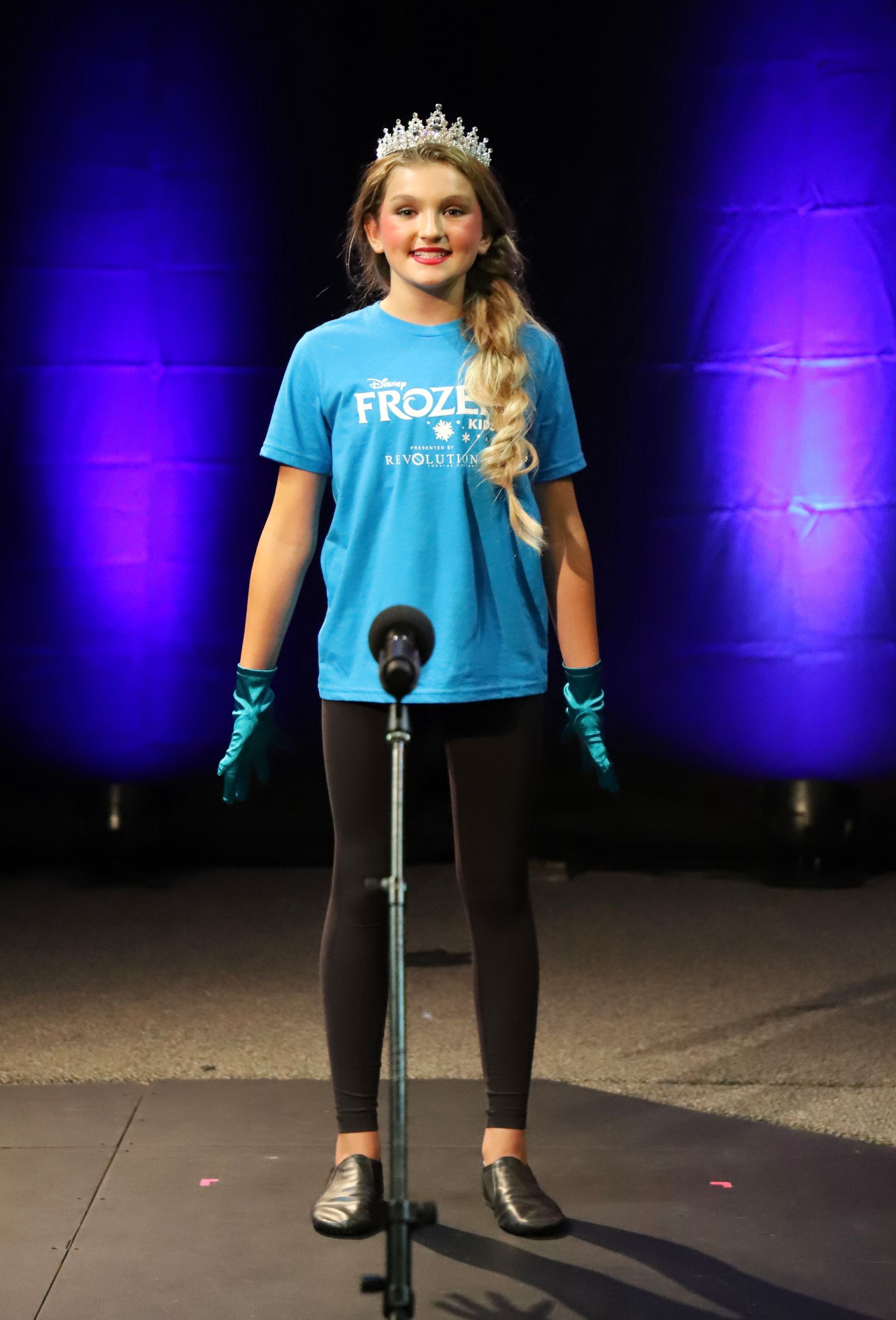 A young girl in a blue shirt is standing in front of a microphone.