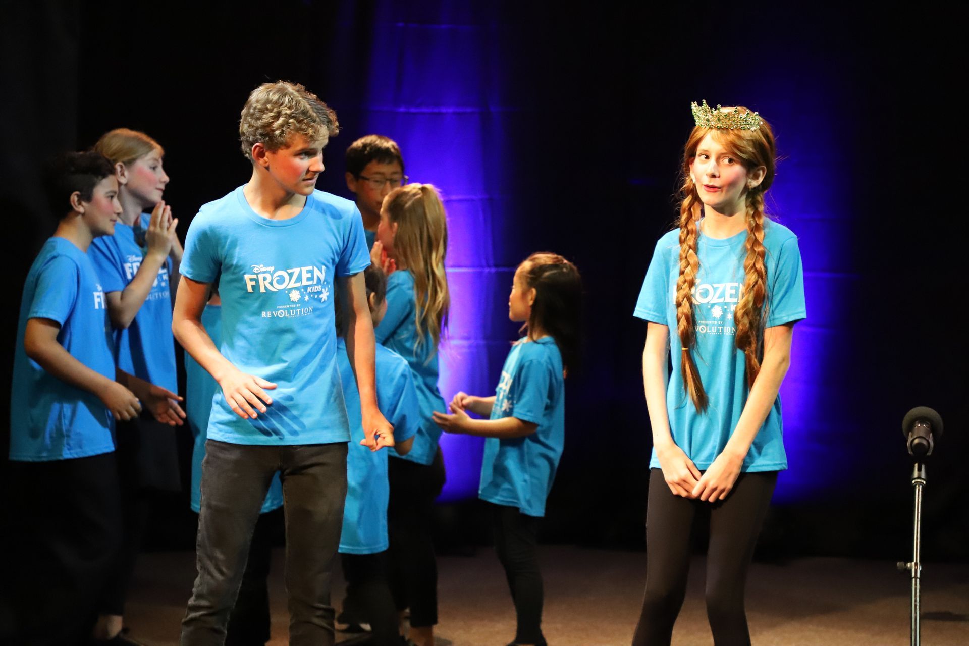 A group of children in blue shirts are standing on a stage.