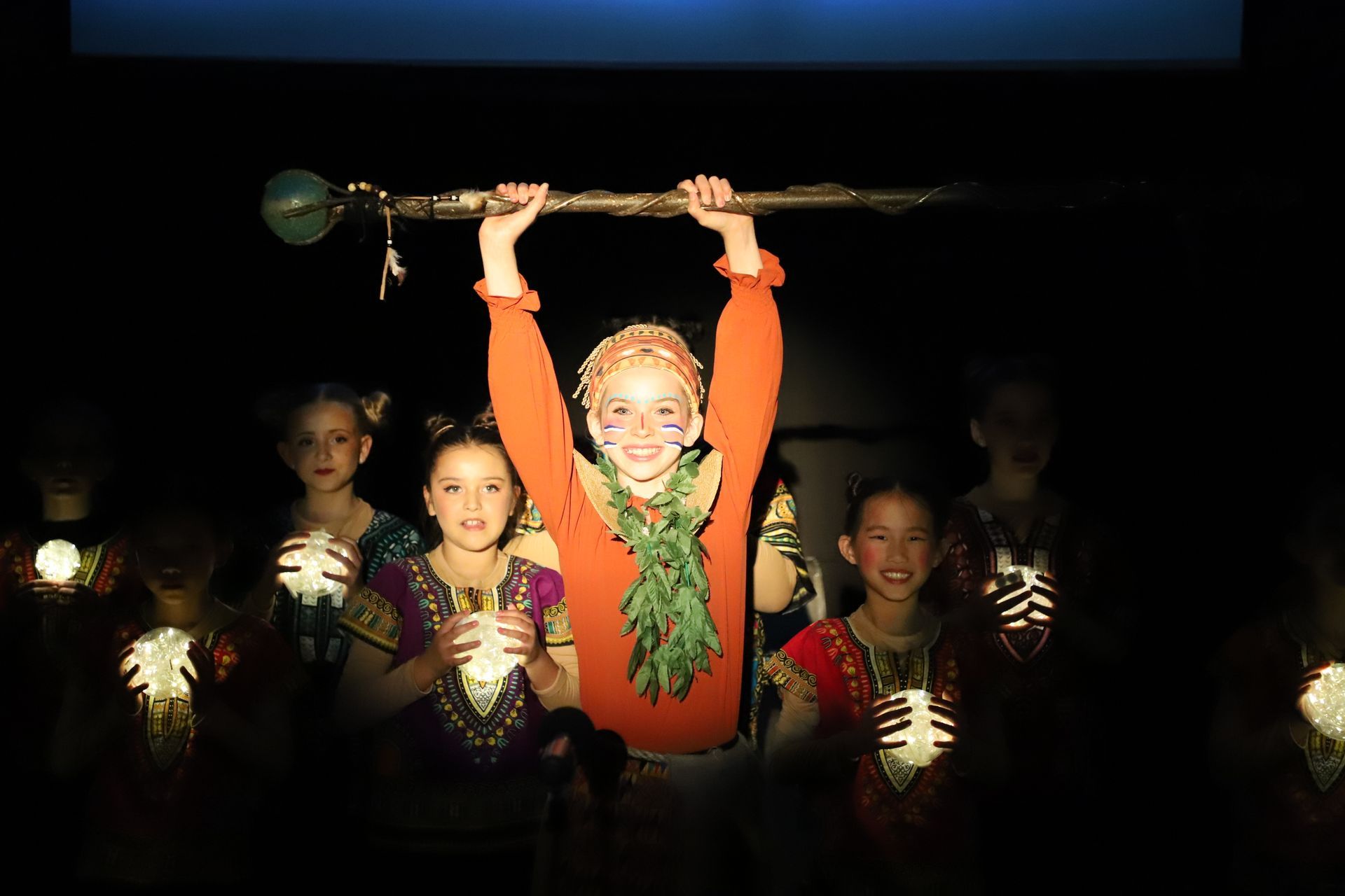 A group of children are standing in a dark room holding candles.