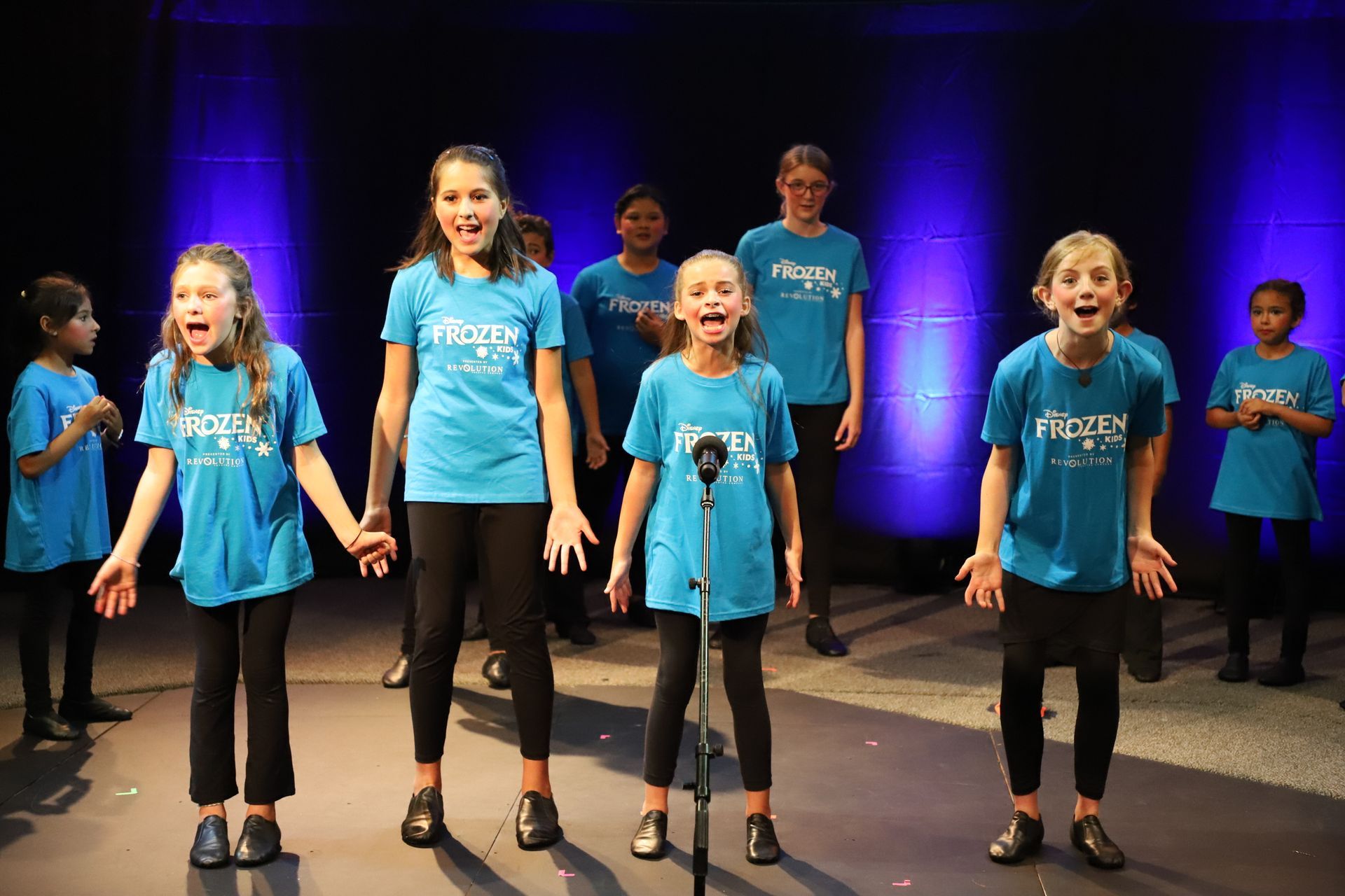 A group of young girls are singing into microphones on a stage.