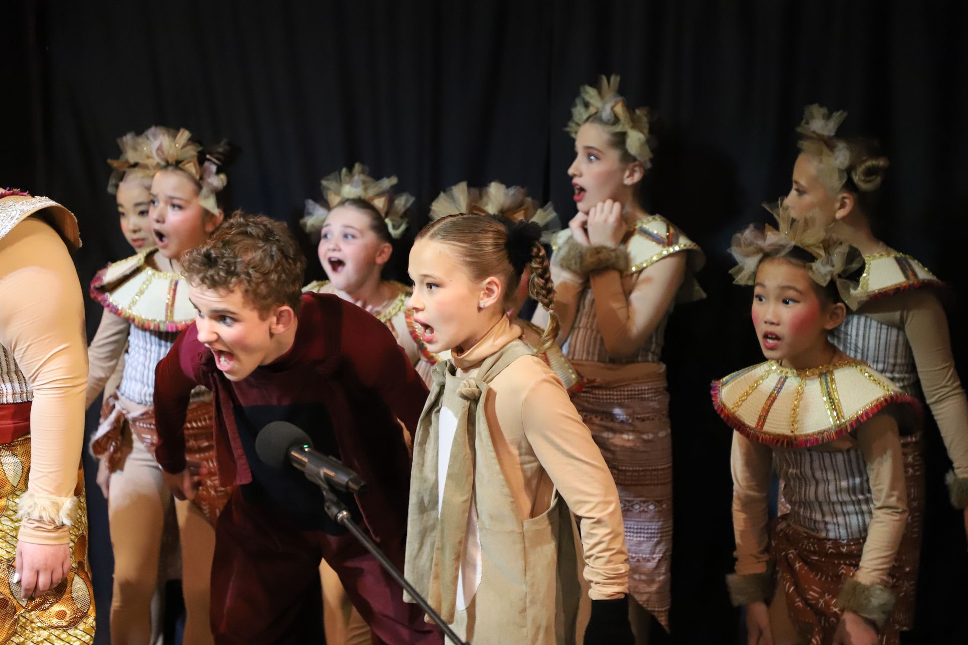 A group of children in costume are singing into a microphone on a stage.