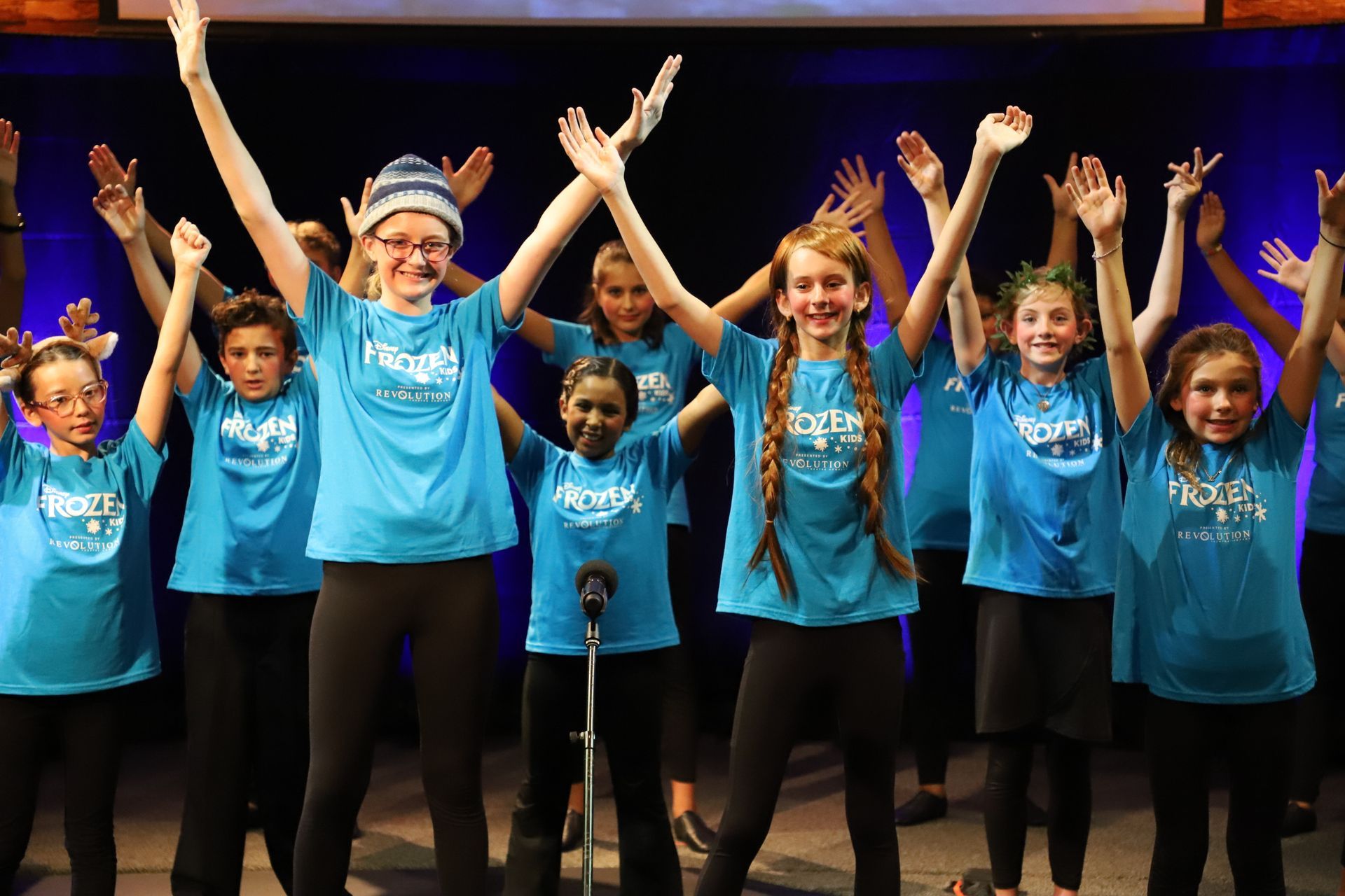 A group of children are standing on a stage with their arms in the air.