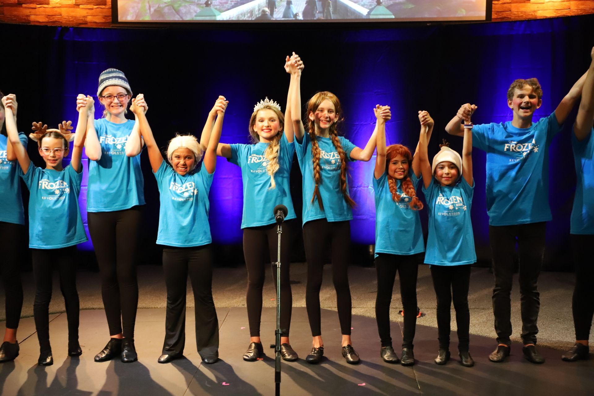 A group of children are holding hands in front of a microphone on a stage.