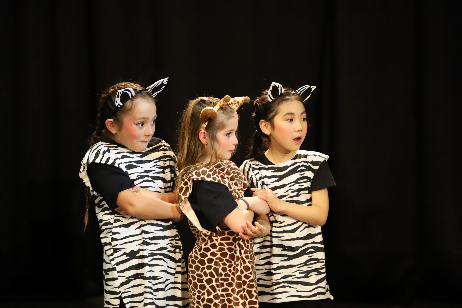 Three young girls dressed as zebras are standing next to each other on a stage.