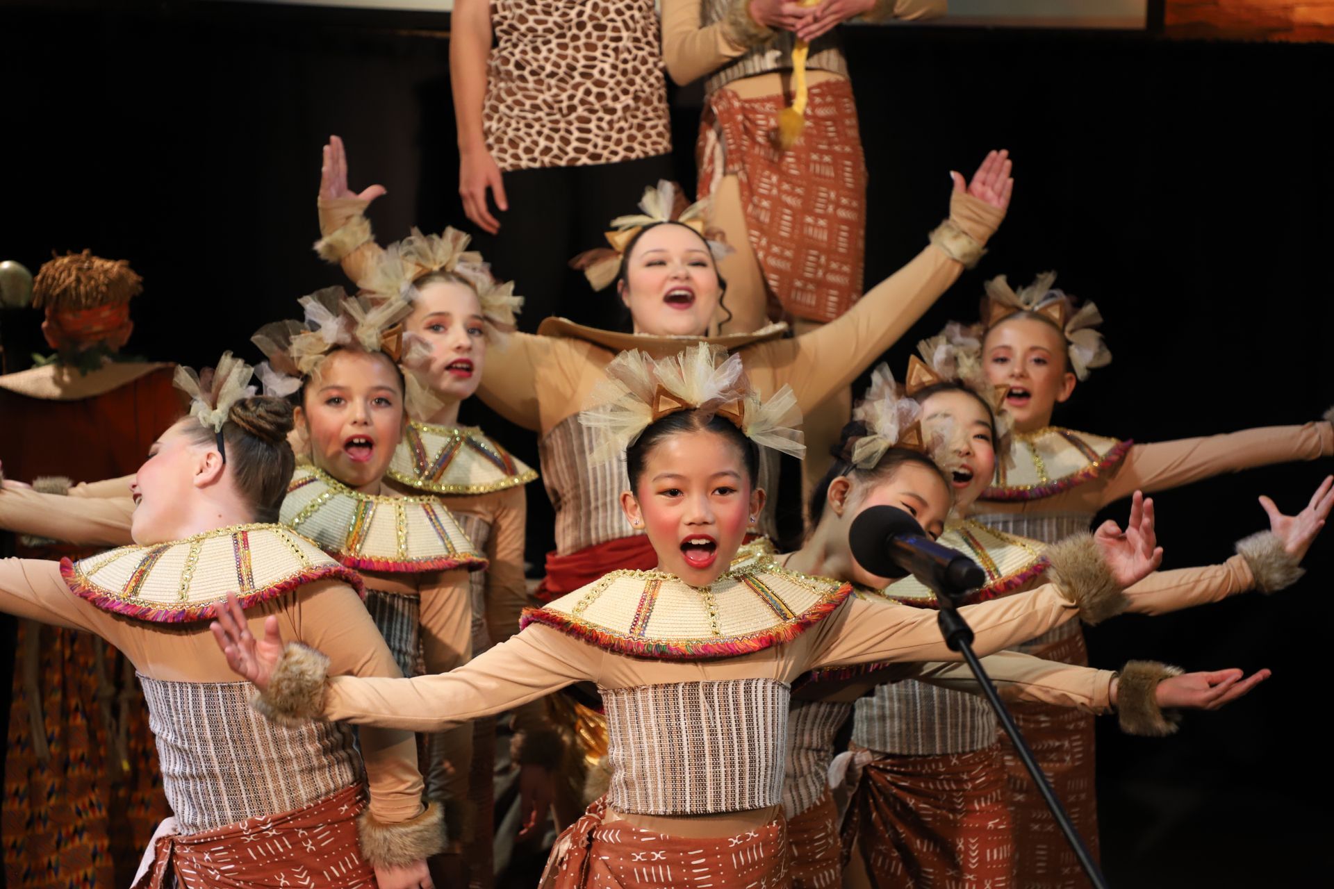 A group of young girls in costume are singing into a microphone.