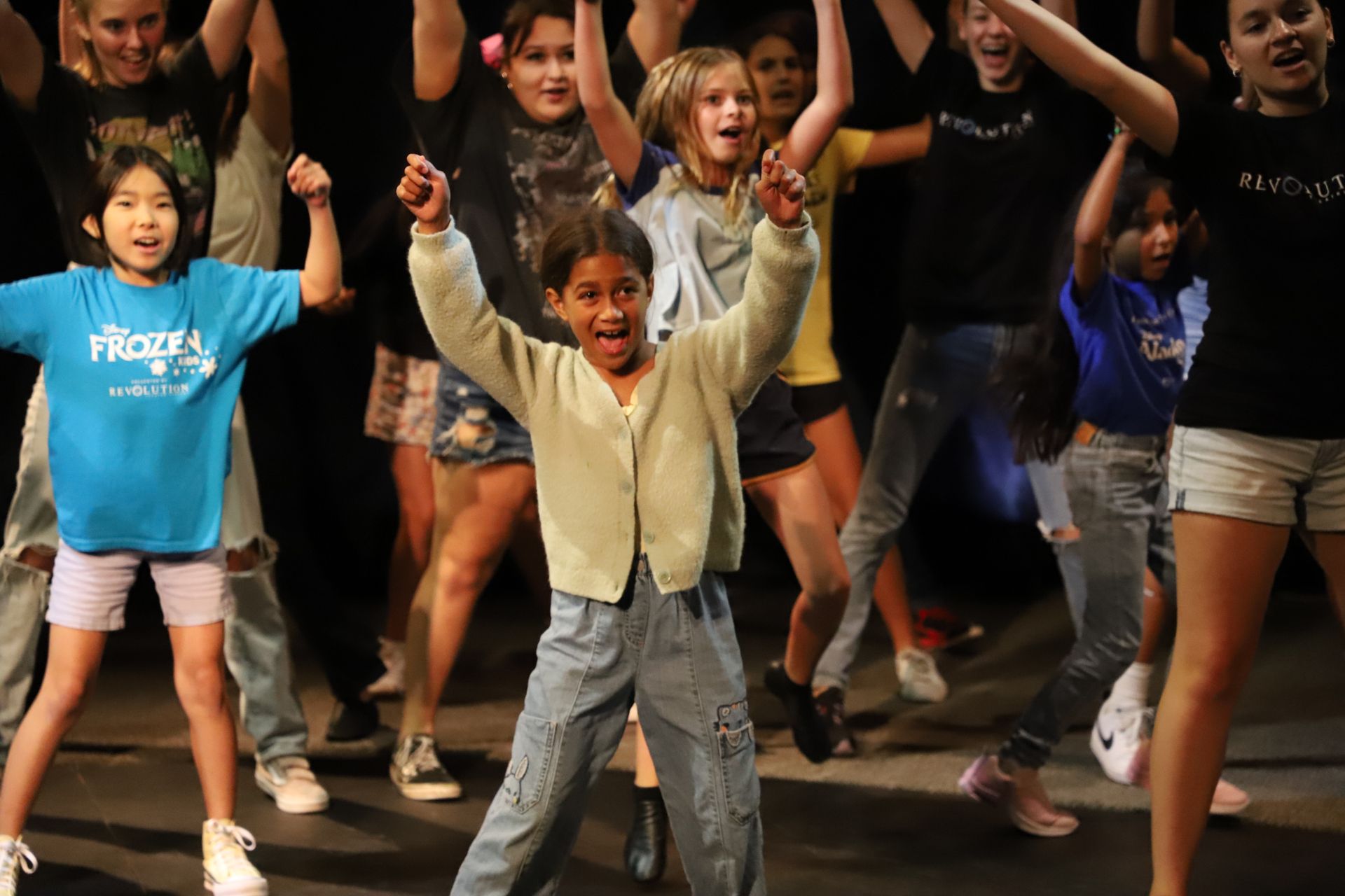 A girl in a blue frozen shirt is dancing with her hands in the air