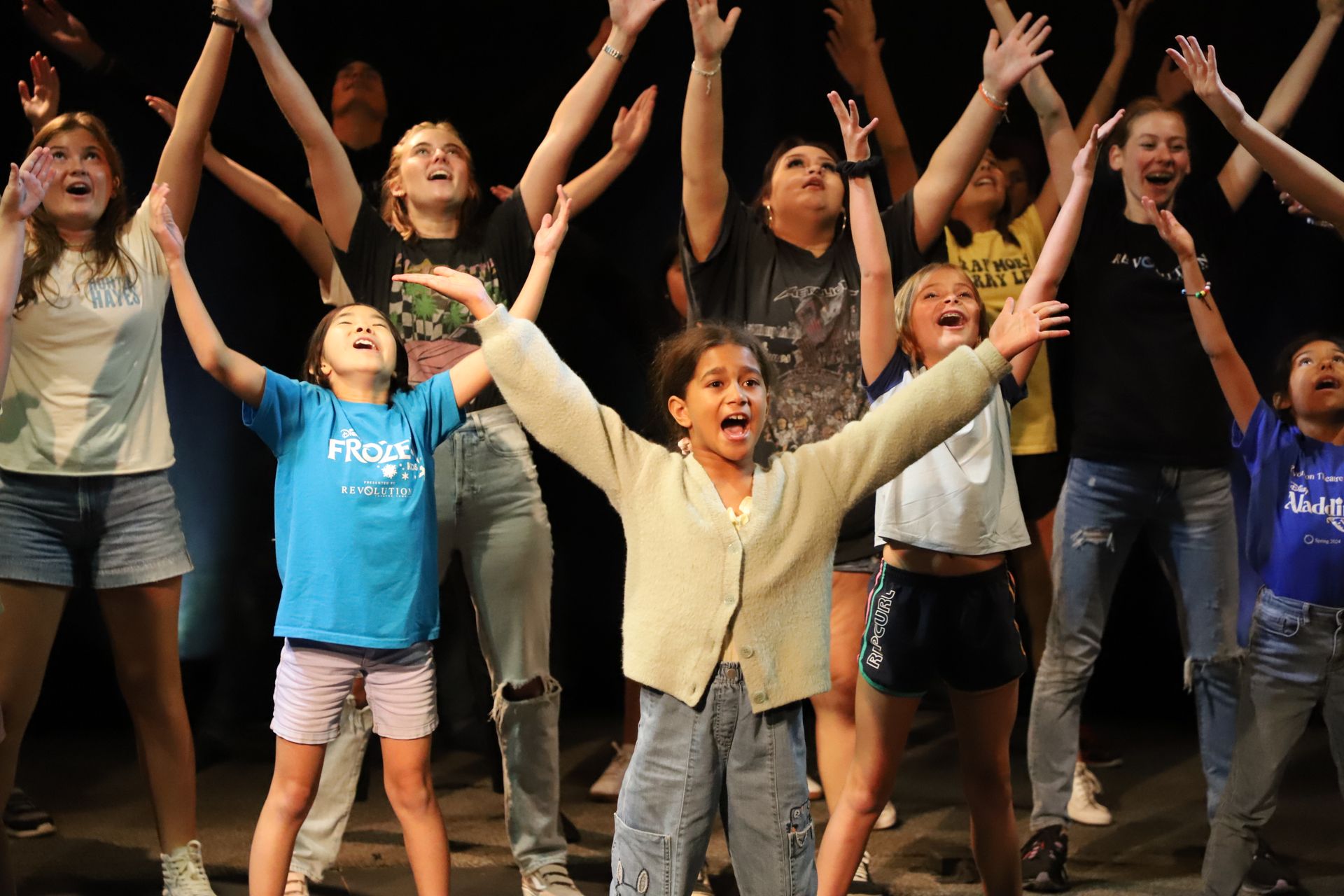 A group of children are standing on a stage with their arms in the air.