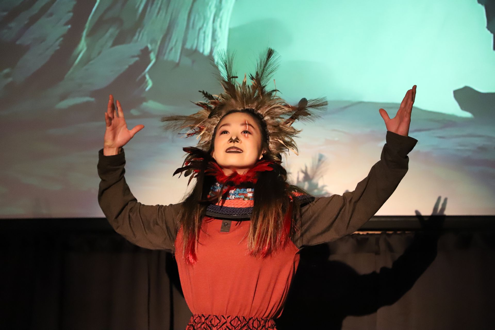 A woman in a native american costume is standing on a stage with her arms outstretched.