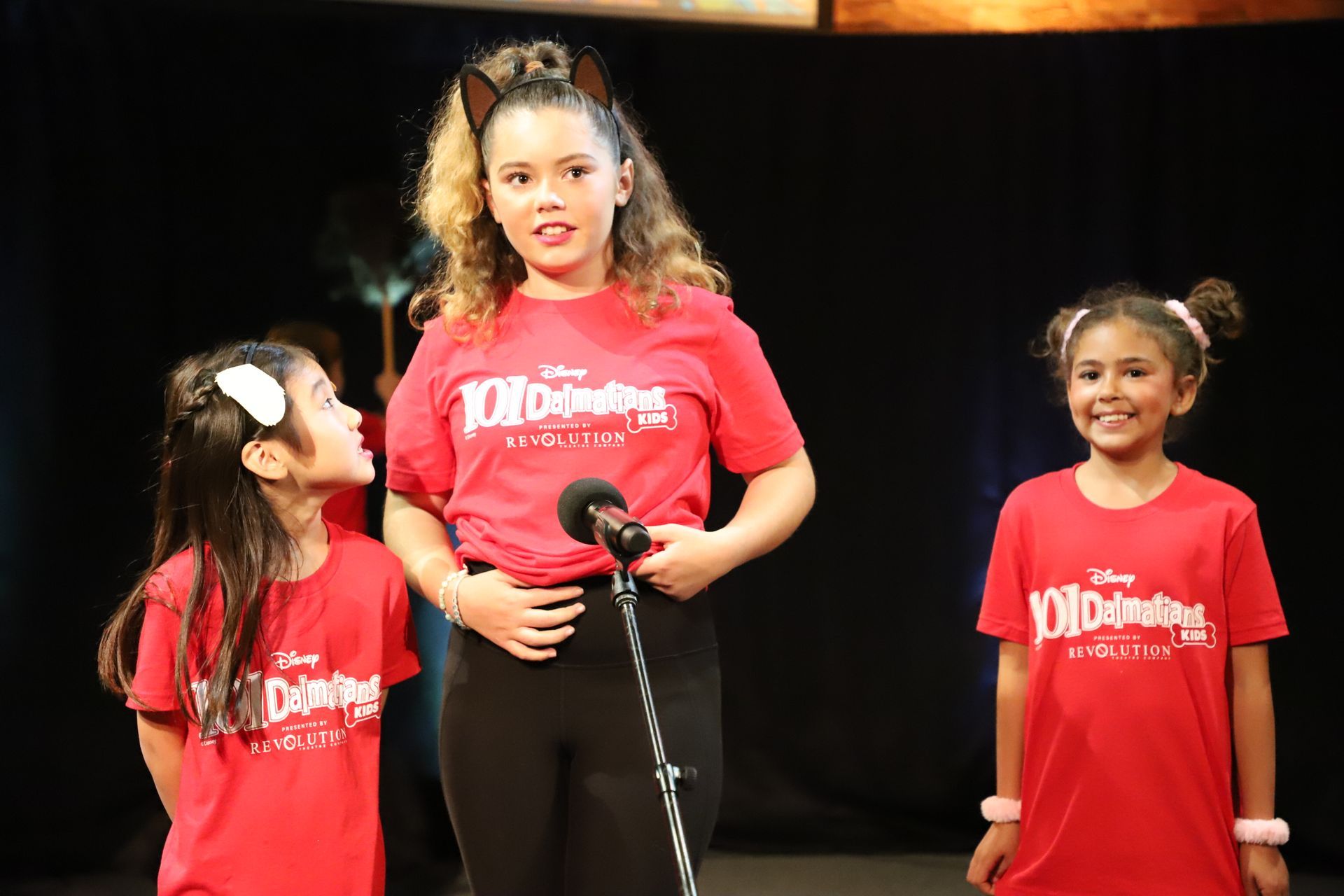 Three young girls wearing red shirts are standing next to each other on a stage.