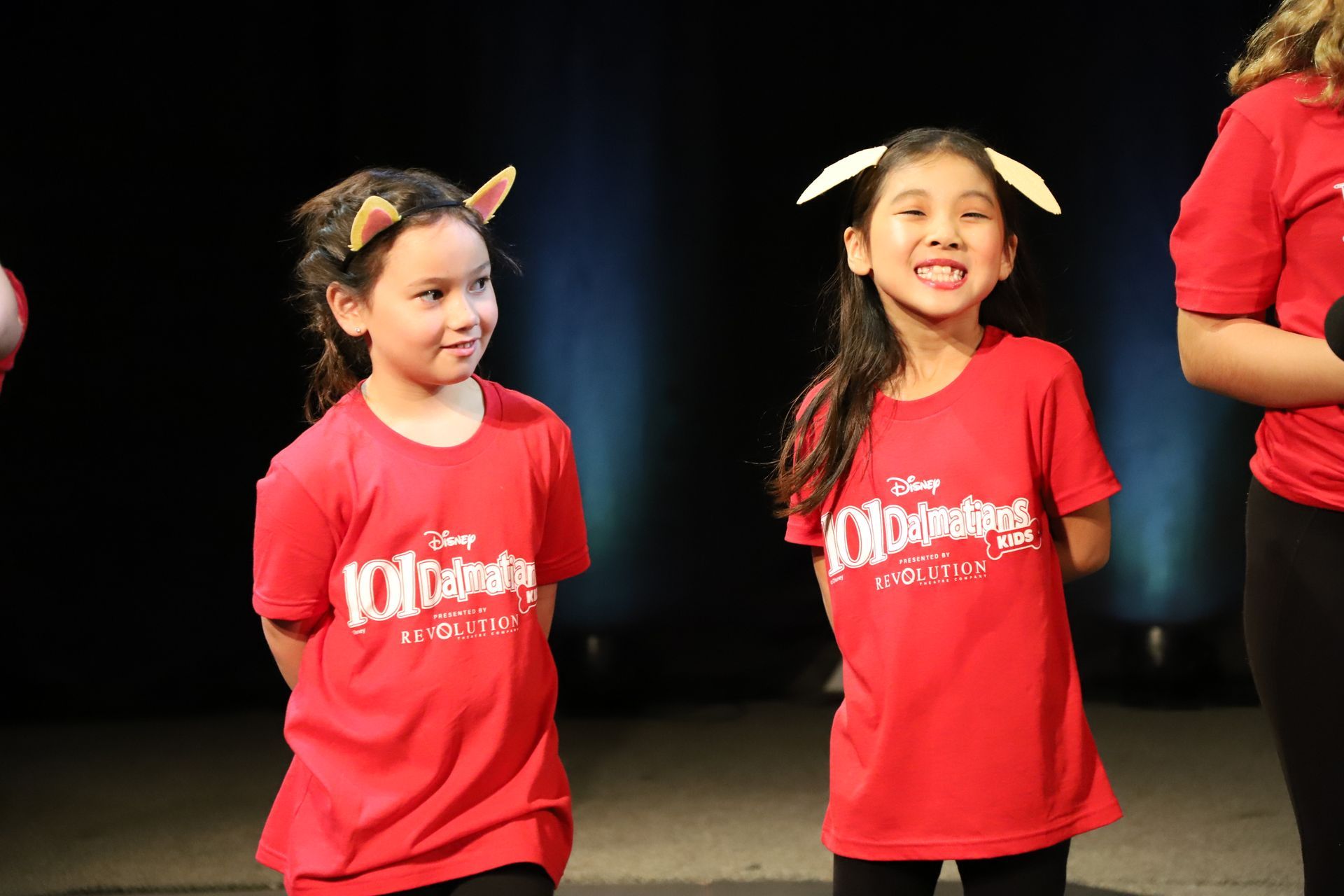Two young girls wearing red shirts that say 101 dalmatians are standing next to each other on a stage.