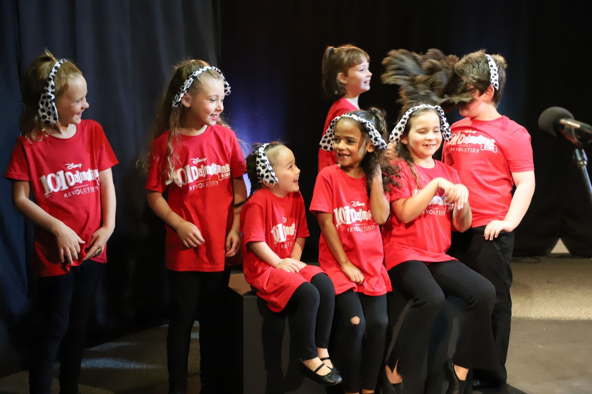 A group of young girls wearing red shirts are sitting in front of a microphone.