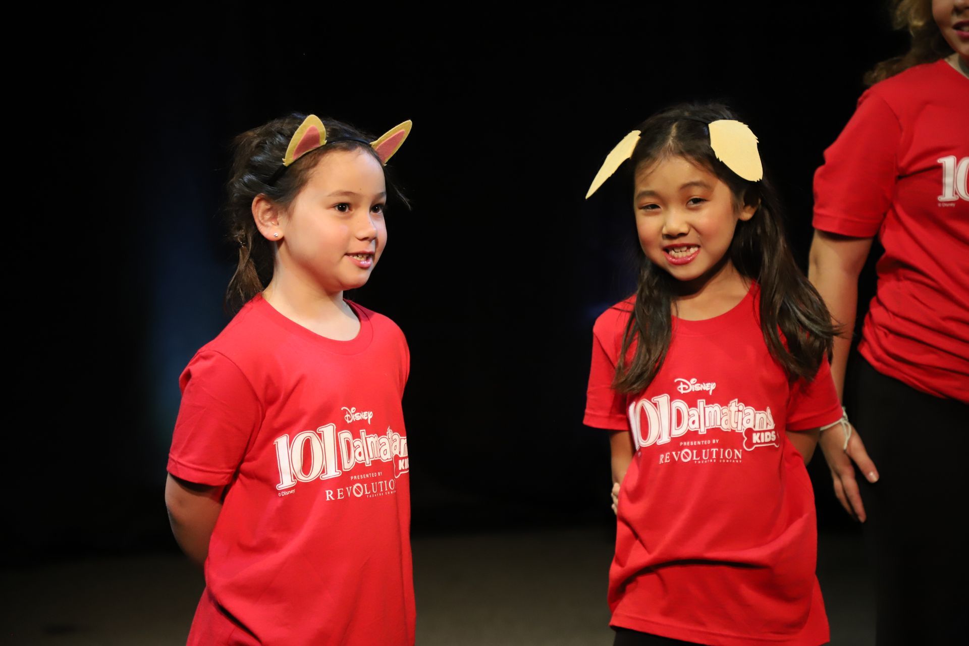 Two young girls in red shirts are standing next to each other on a stage.