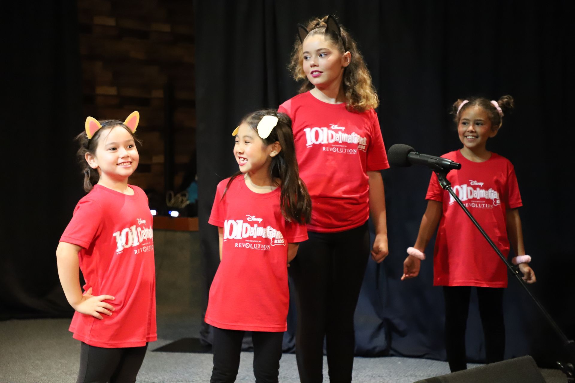 A group of young girls wearing red shirts are singing into a microphone.