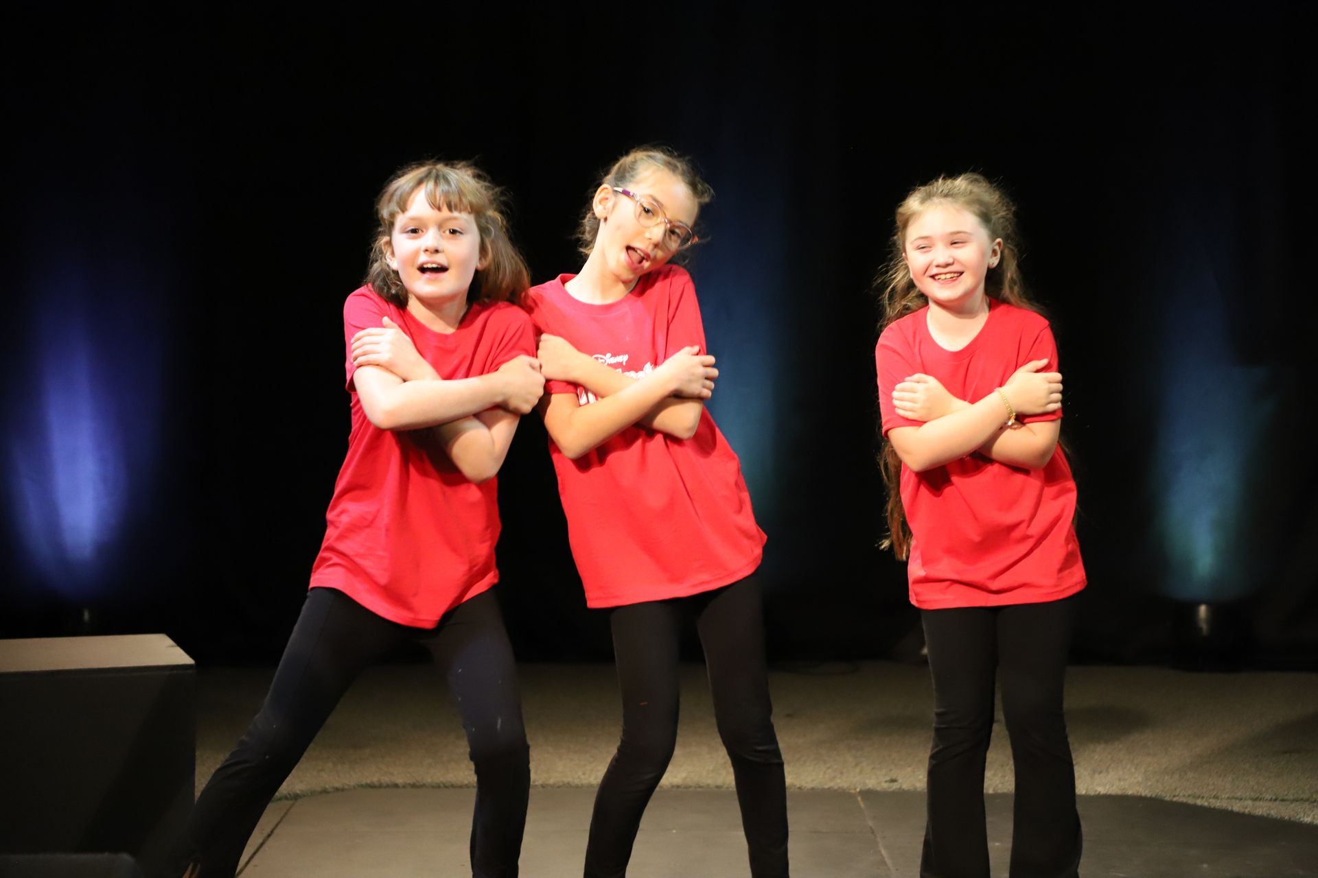 Three young girls in red shirts are standing next to each other on a stage.