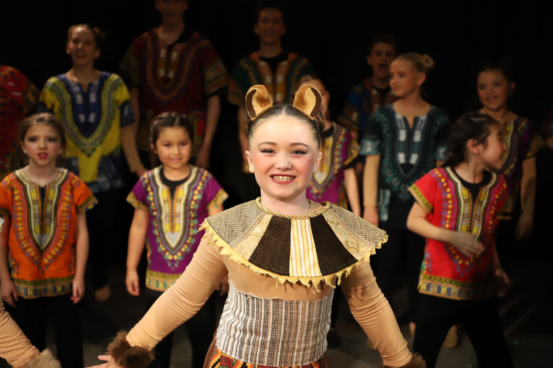 A girl in a lion costume is standing in front of a group of children.