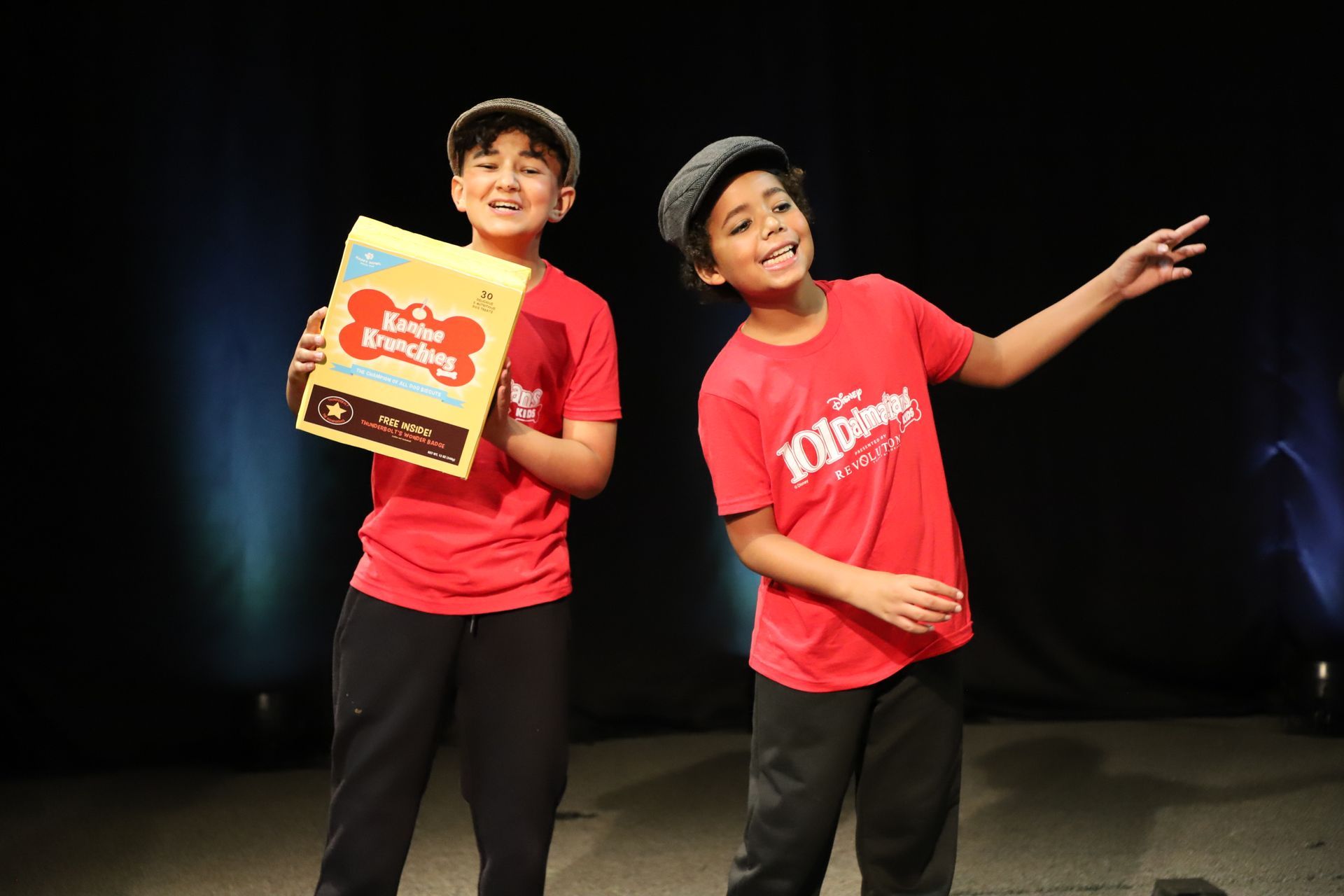 Two young boys are standing next to each other on a stage holding a box of cereal.
