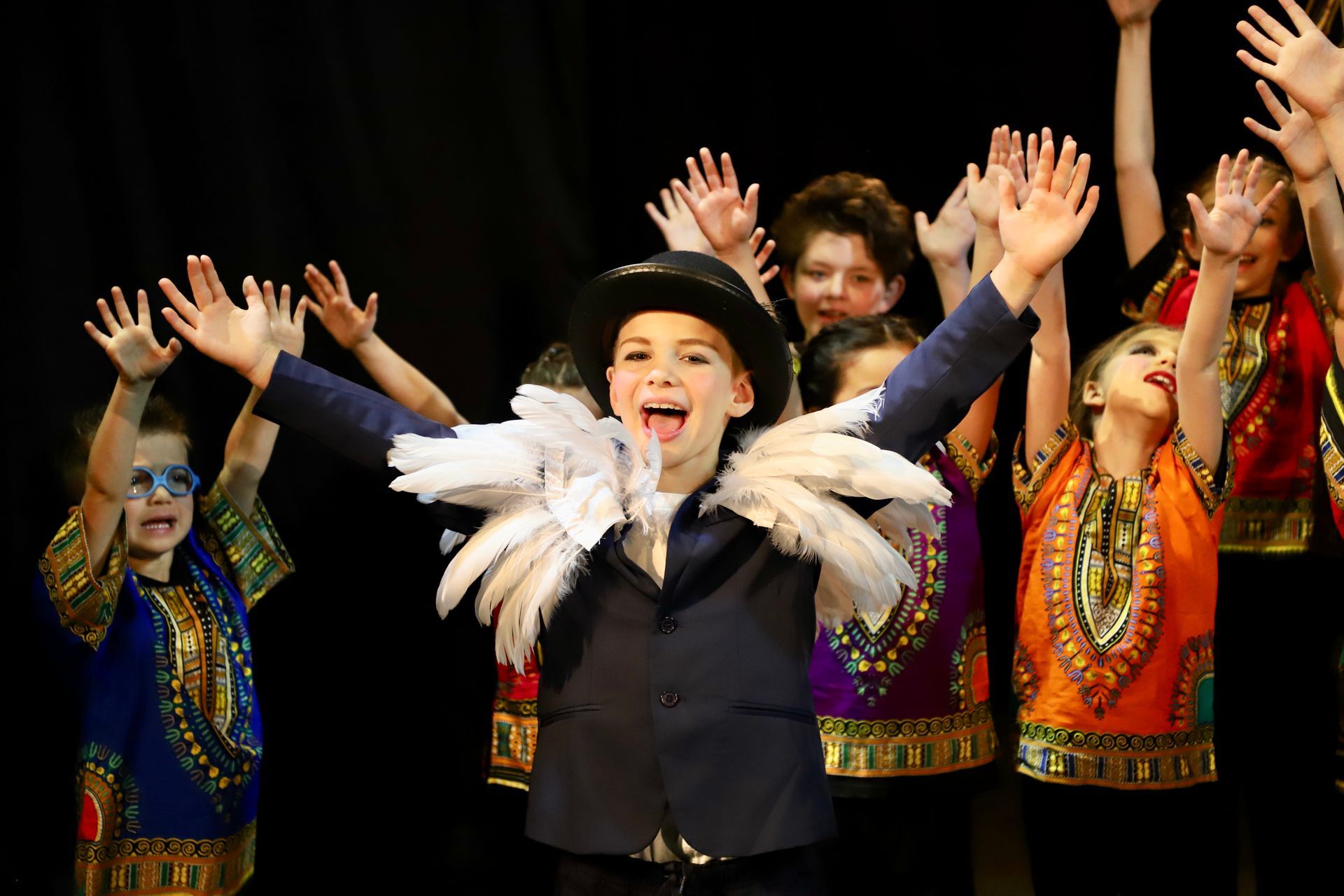 A group of children are dancing on a stage with their hands in the air.