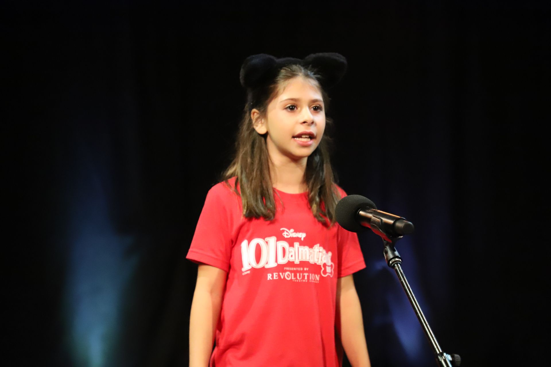 A young girl in a red shirt is singing into a microphone.