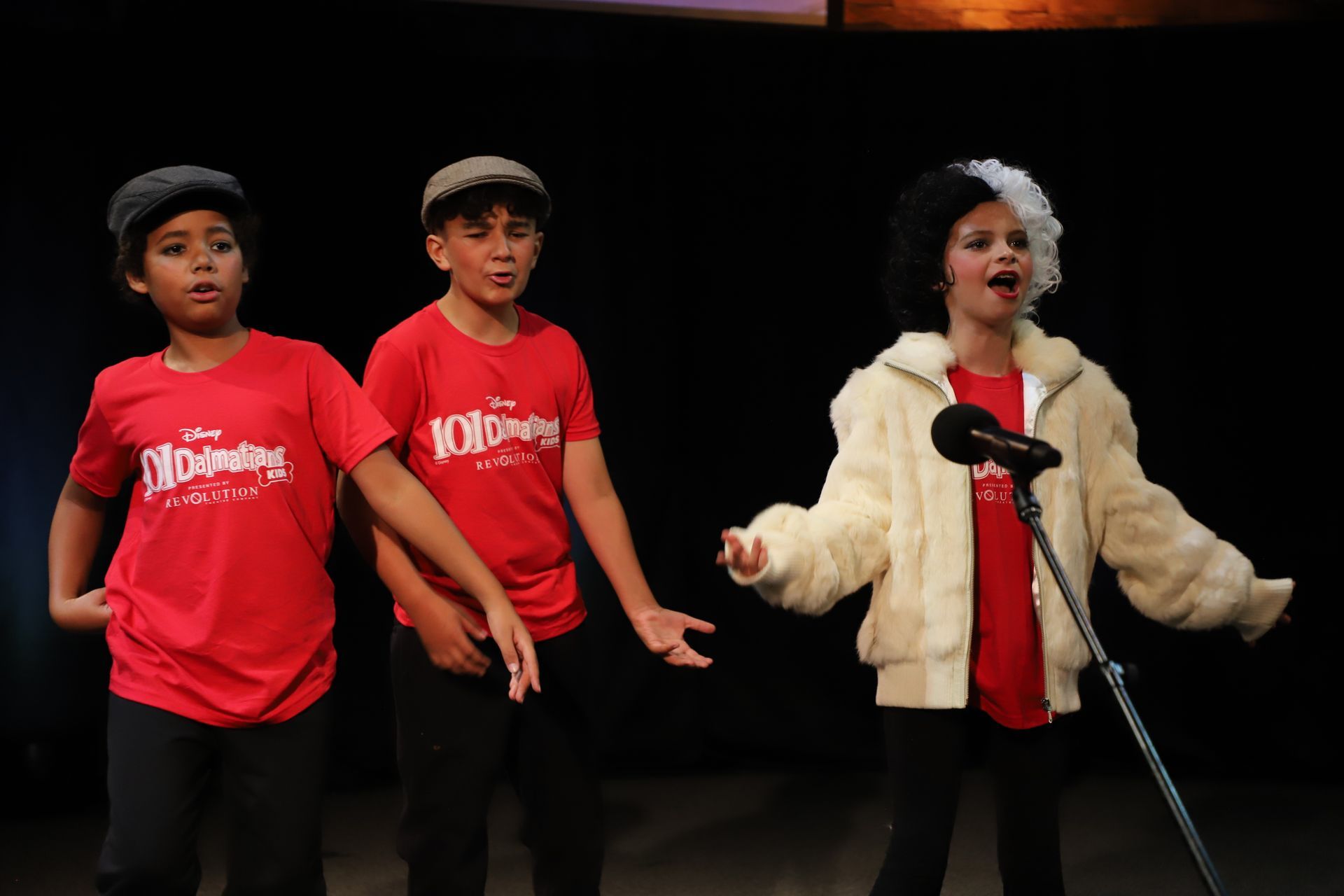 Three young boys are singing into a microphone on a stage.