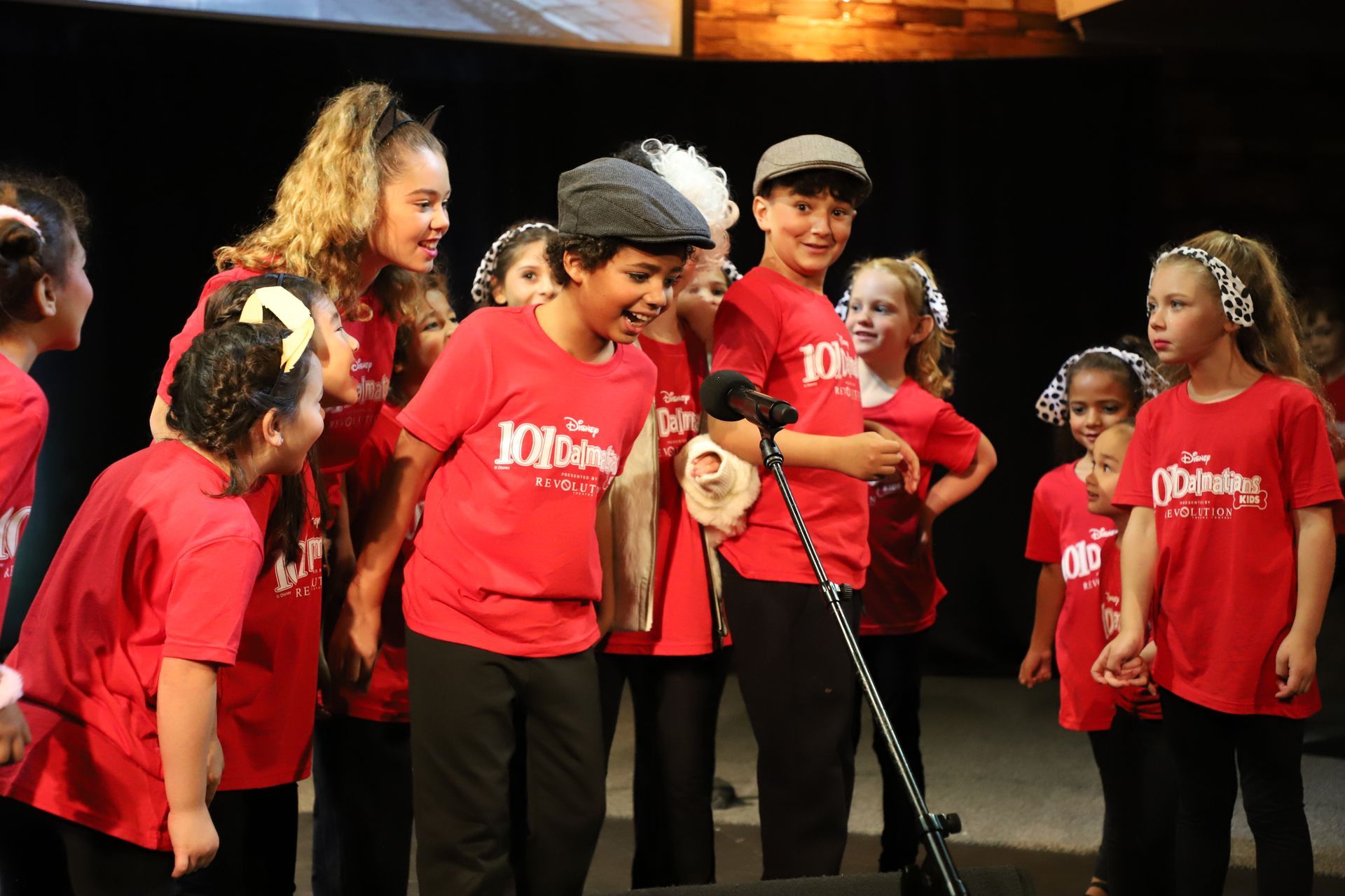 A group of children in red shirts are standing around a microphone.