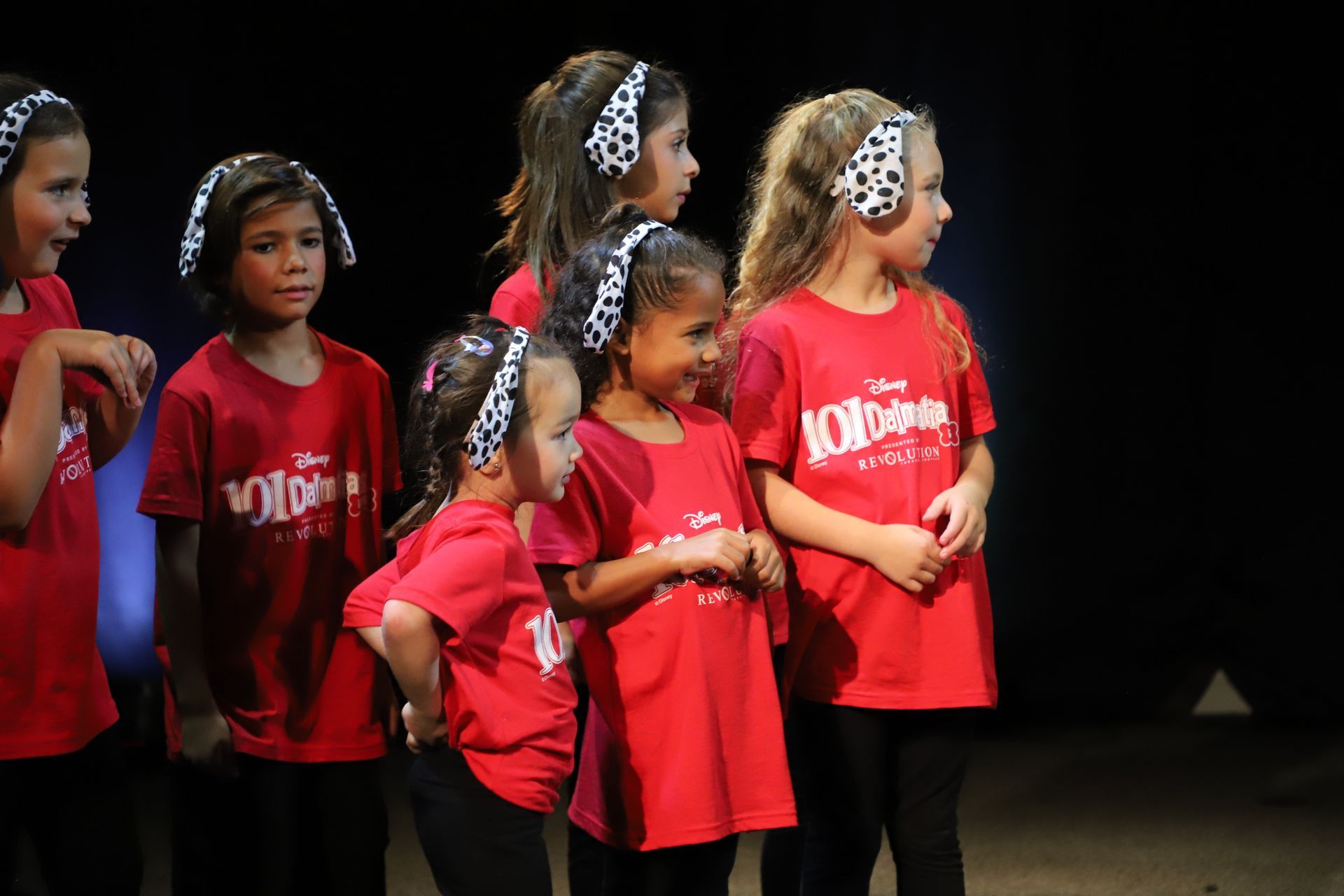 A group of young girls wearing red shirts and headbands are standing on a stage.