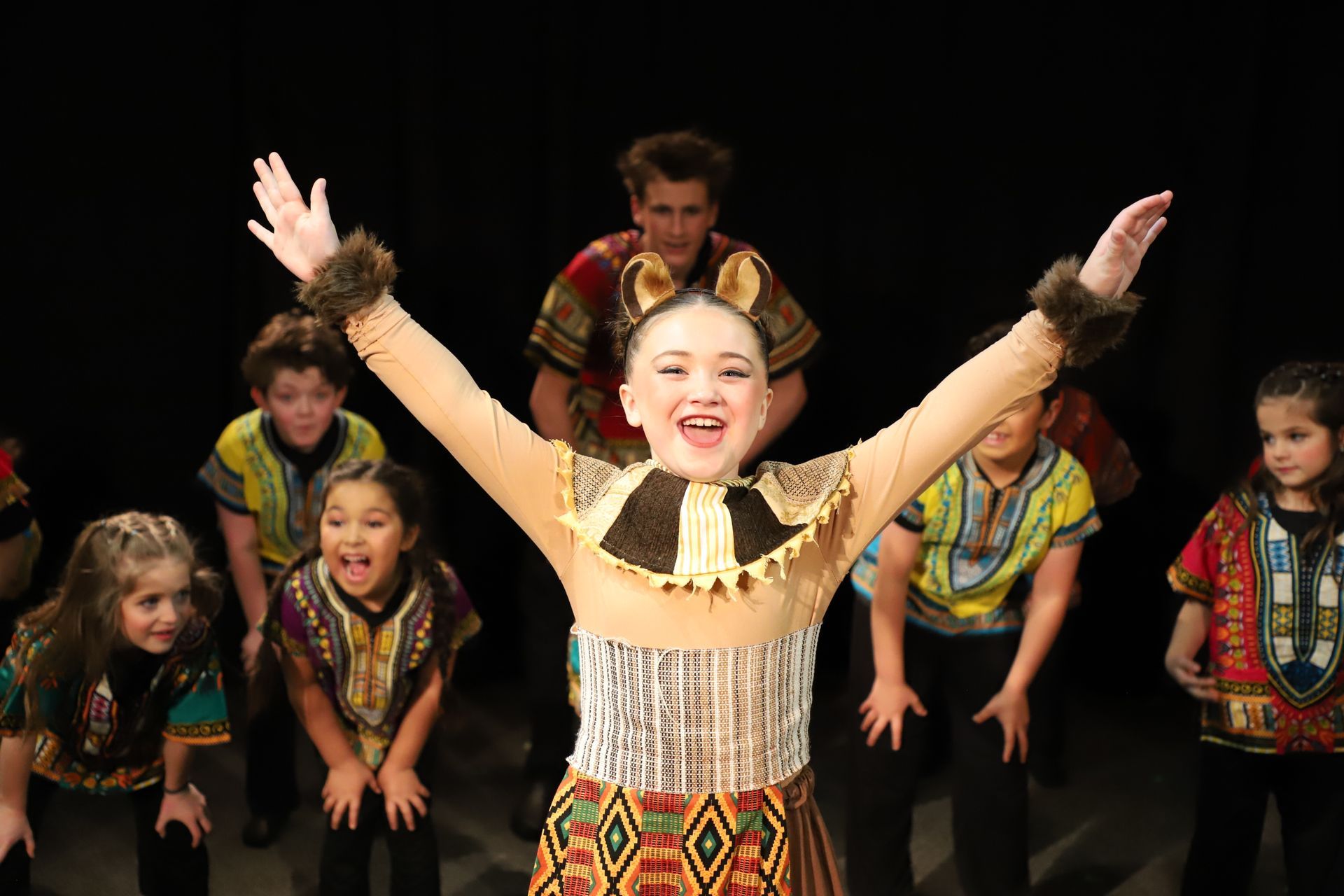 A girl in a lion costume is standing in front of a group of children.
