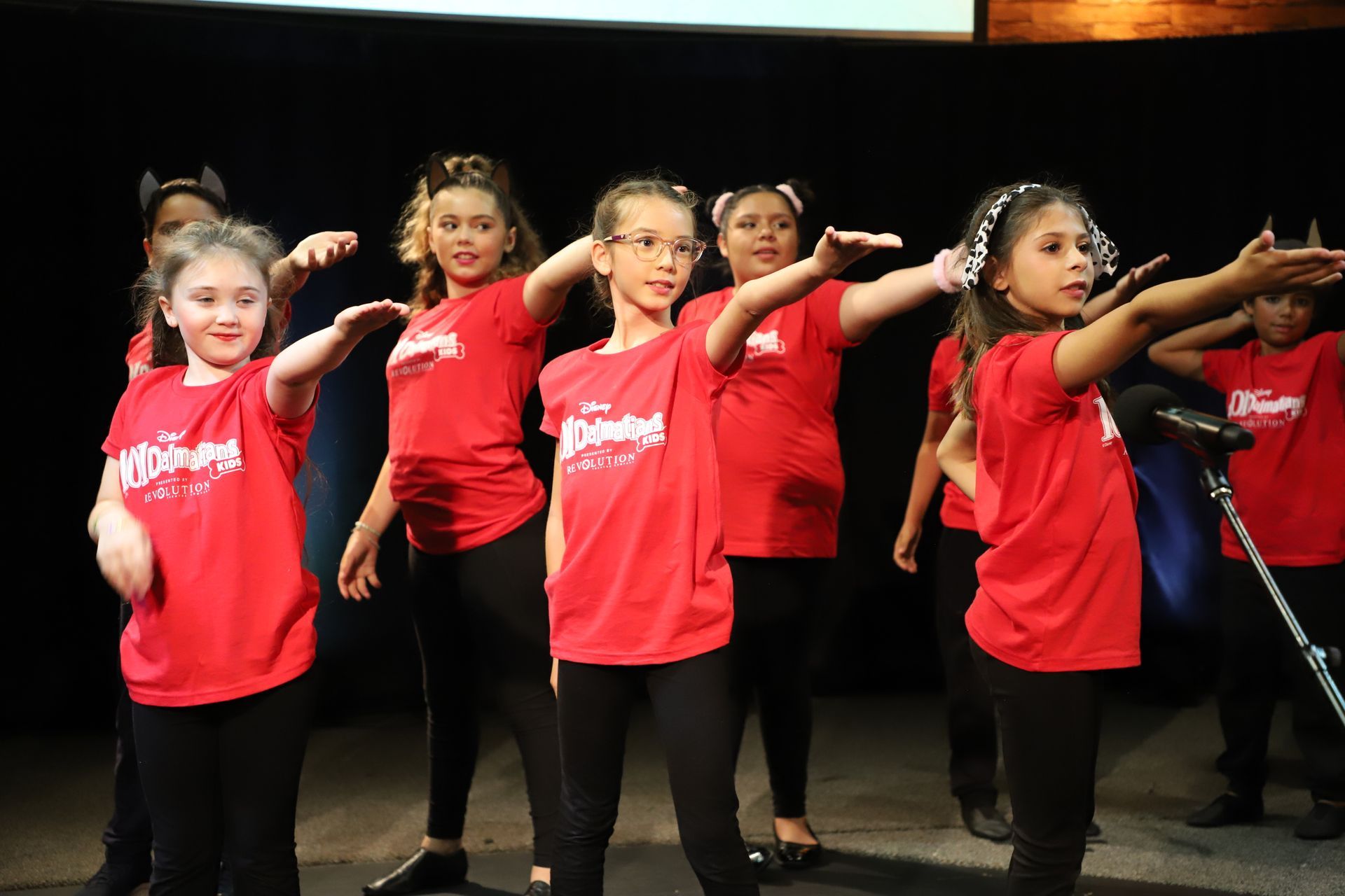 A group of young girls in red shirts are dancing on a stage.