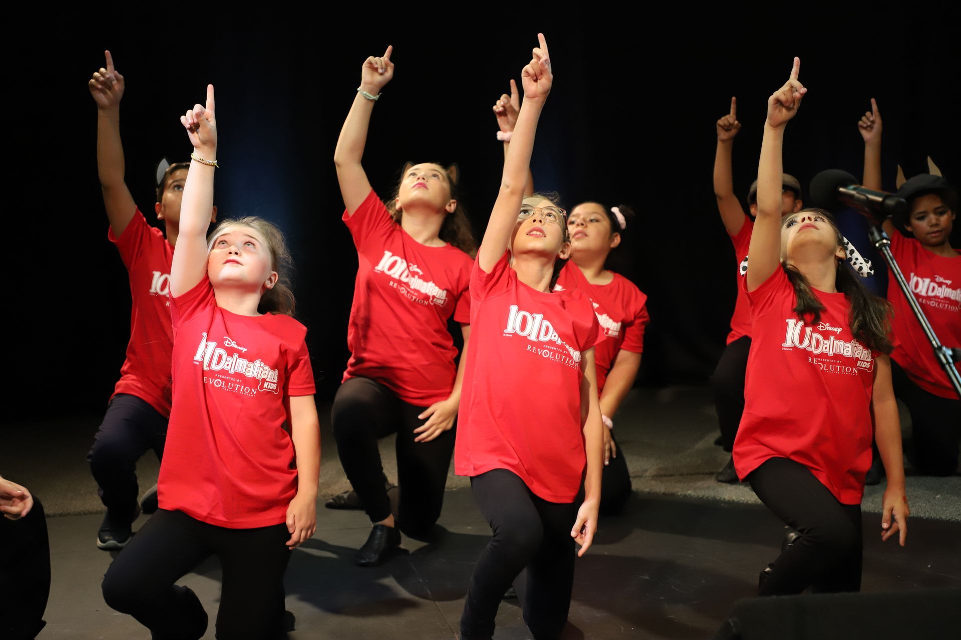A group of young girls in red shirts are dancing on a stage.