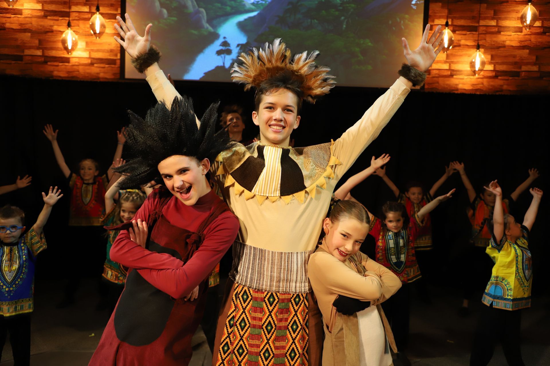 A group of children are standing on a stage with their arms in the air.