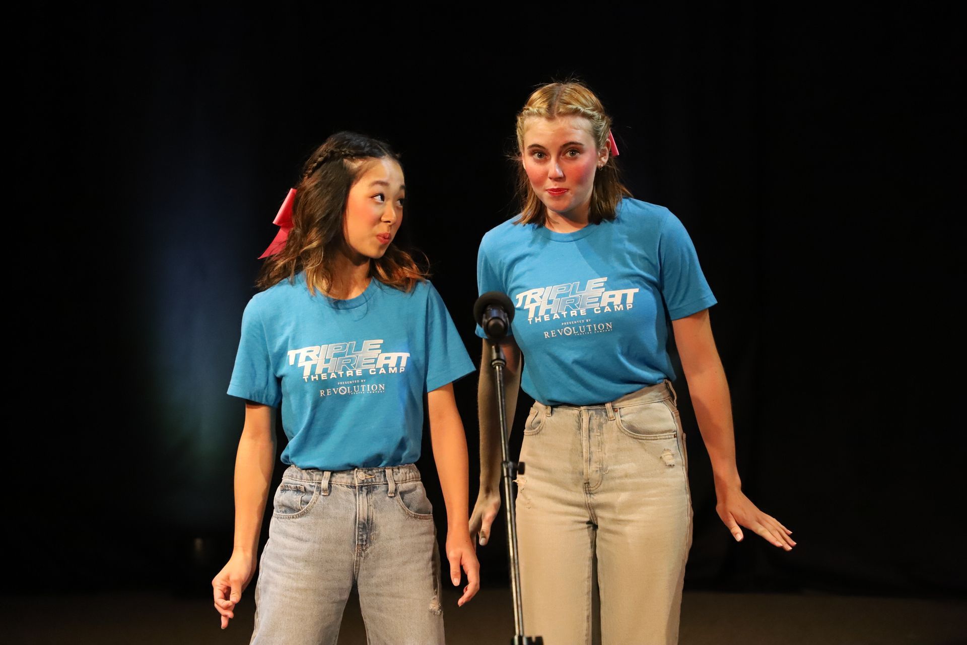 Two girls in blue shirts are standing next to each other on a stage.