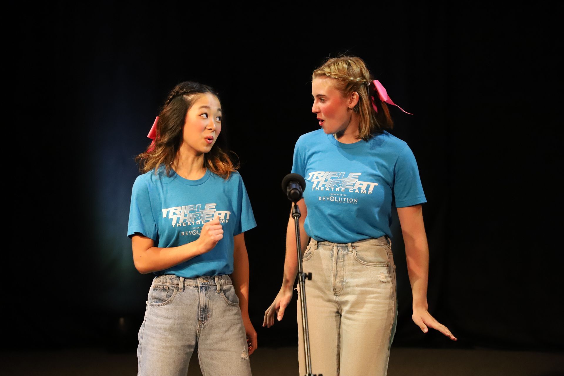 Two young women are standing next to each other on a stage in front of a microphone.