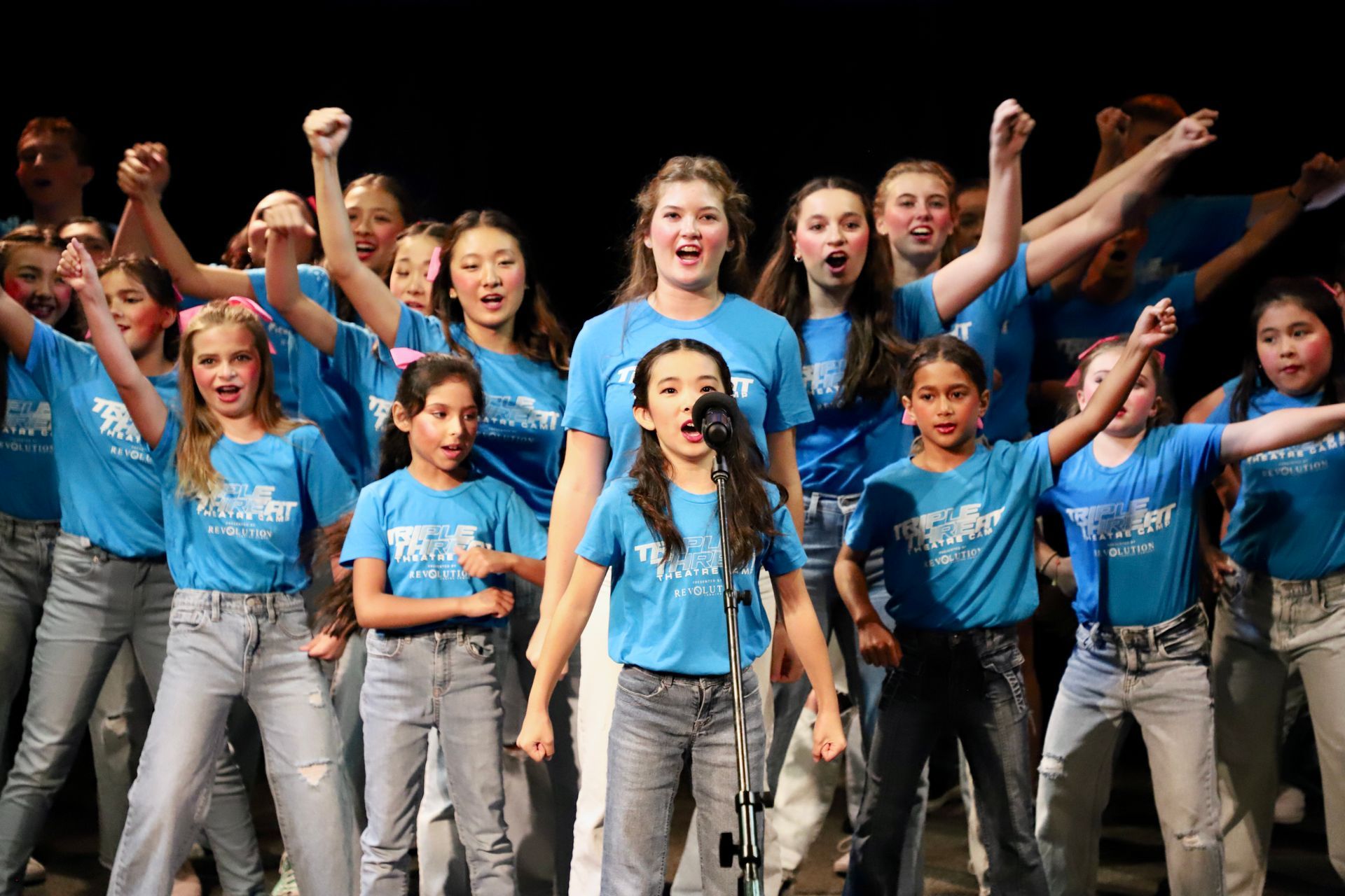 A group of young girls are singing into a microphone on a stage.