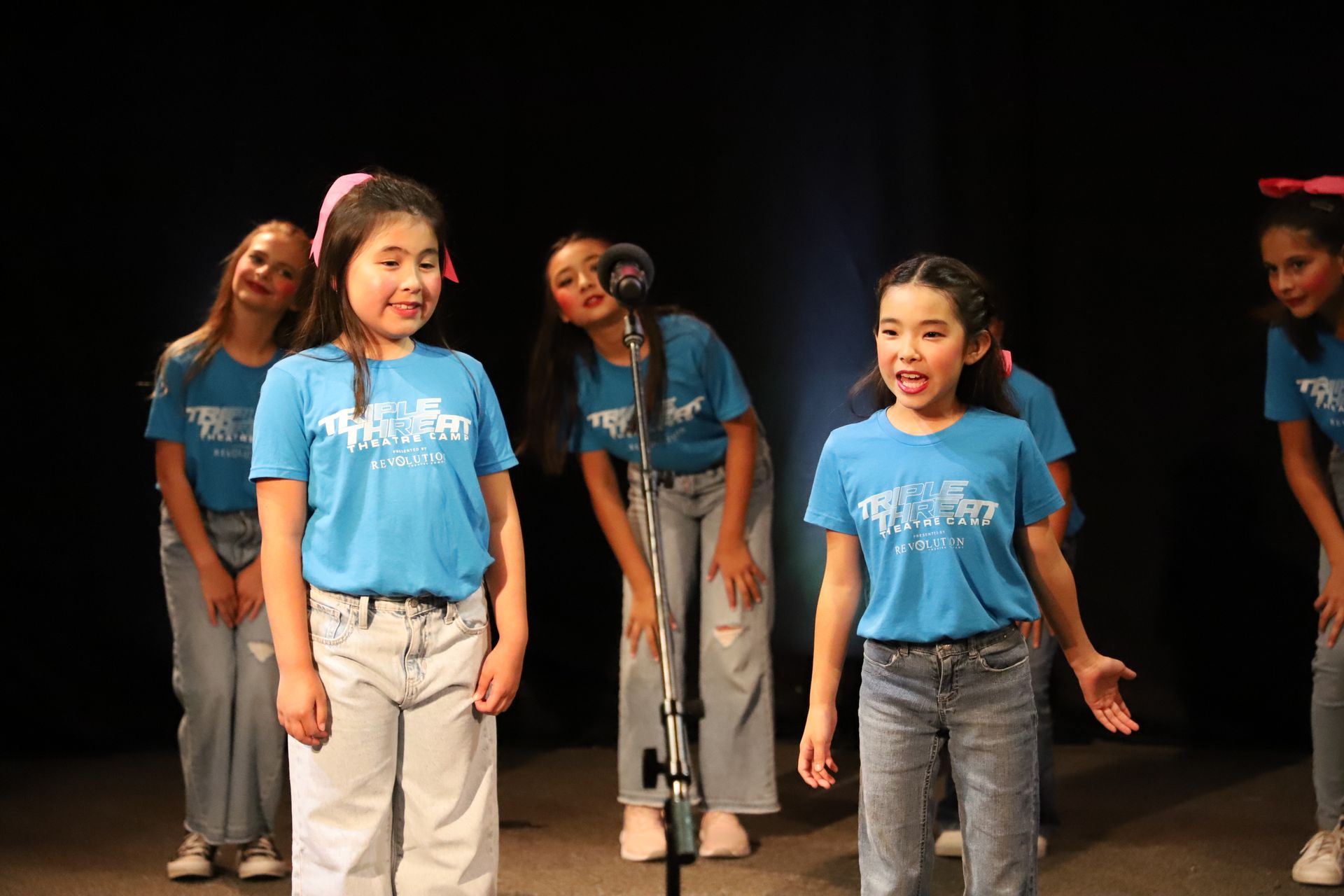 A group of young girls are singing into microphones on a stage.