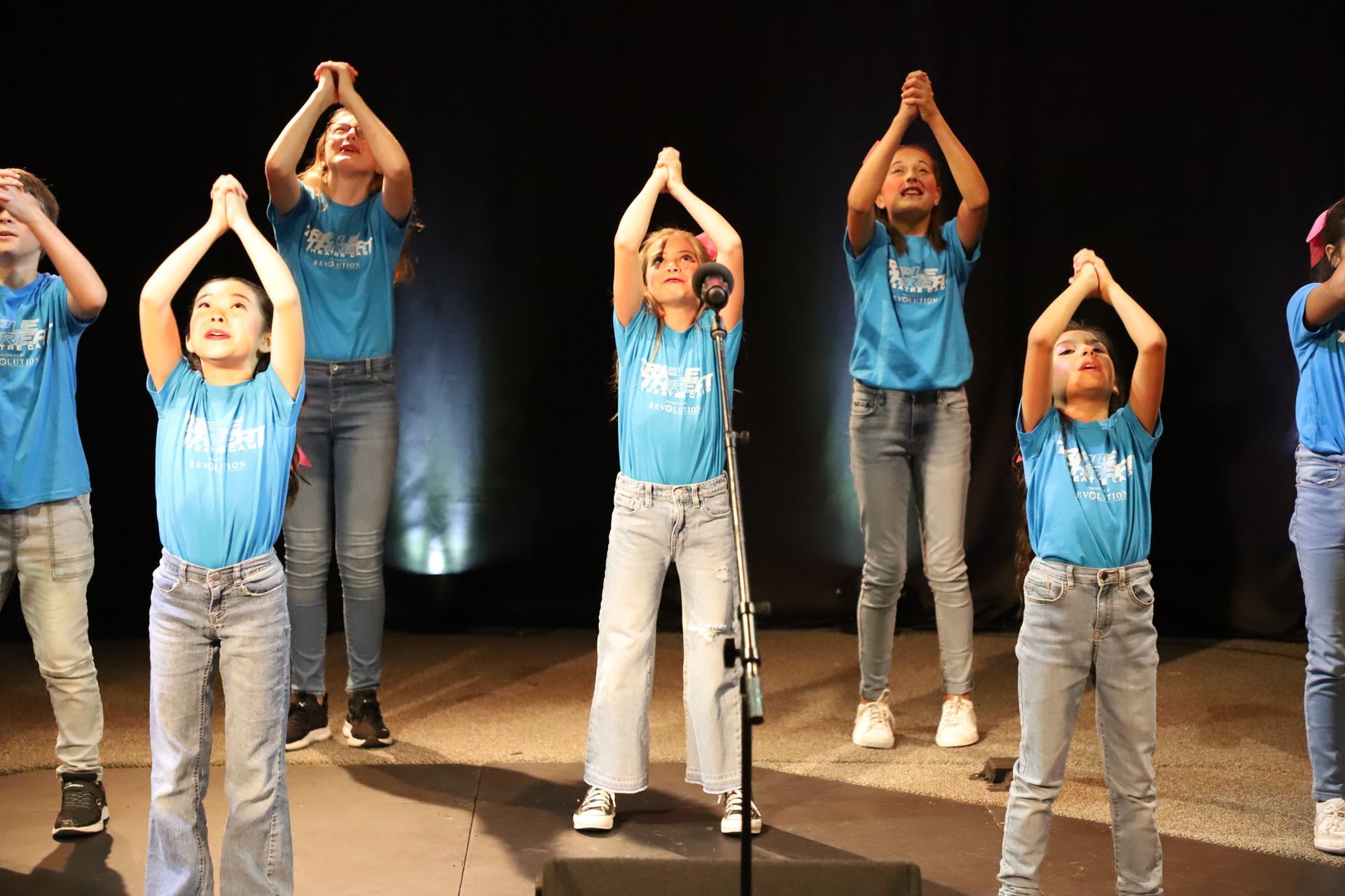 A group of young girls are singing into a microphone on a stage.