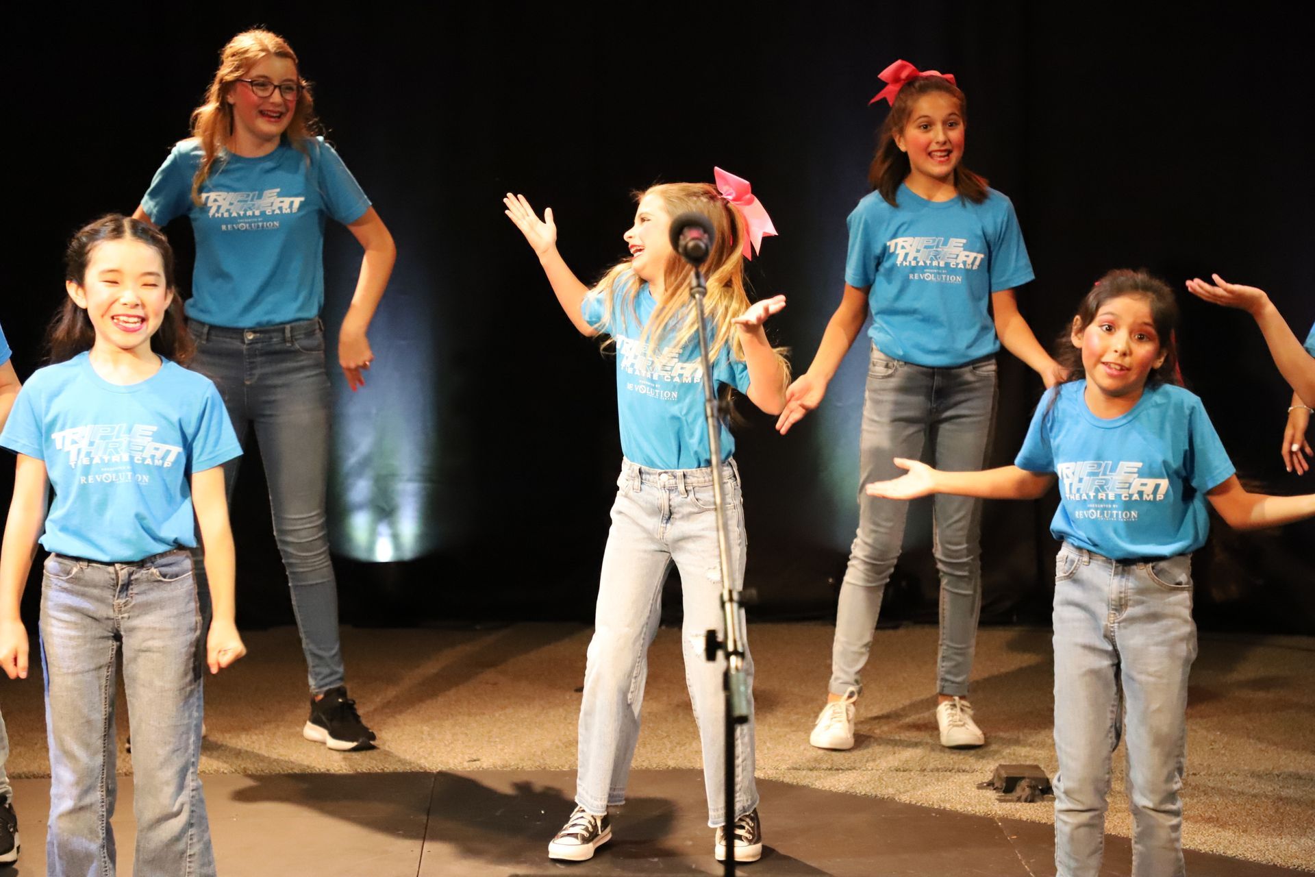 A group of young girls are singing into a microphone on a stage.