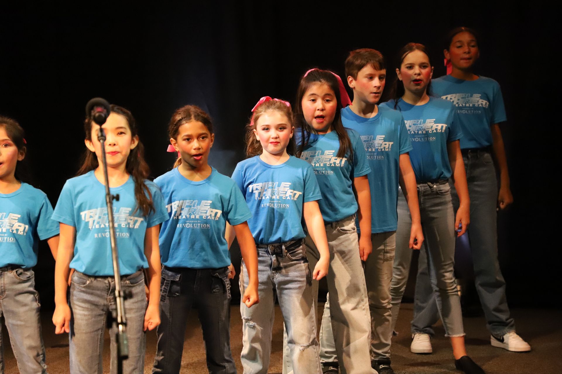 A group of children are singing into microphones on a stage.