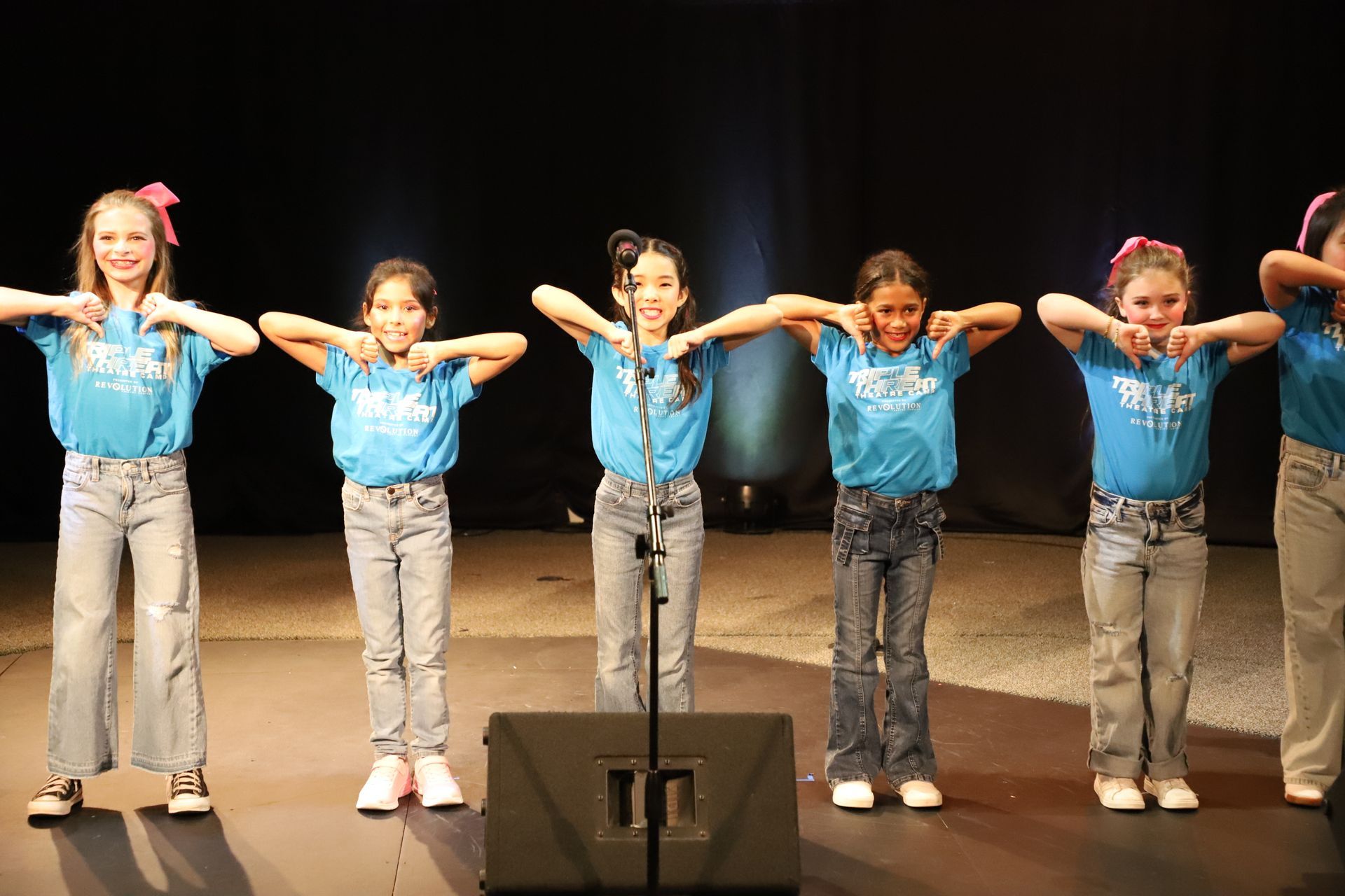 A group of young girls are standing in front of a microphone on a stage.