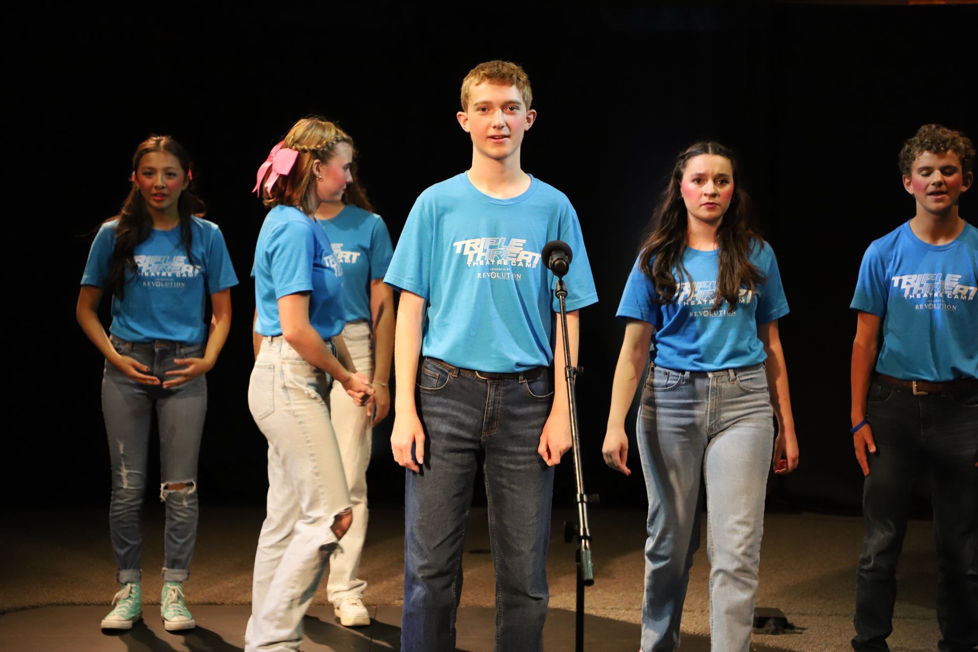 A group of young people are standing in front of a microphone on a stage.