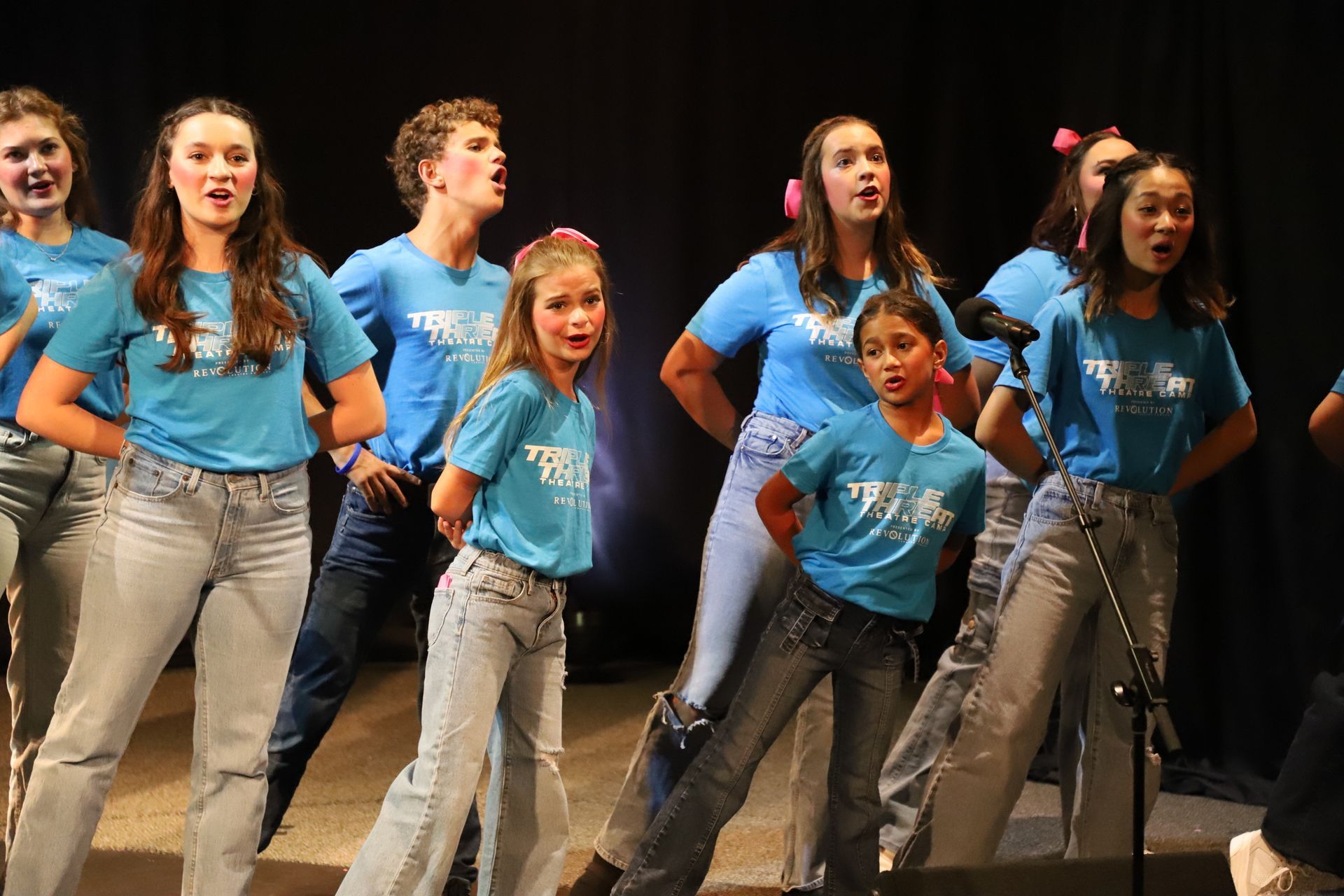 A group of young people are singing into microphones on a stage.
