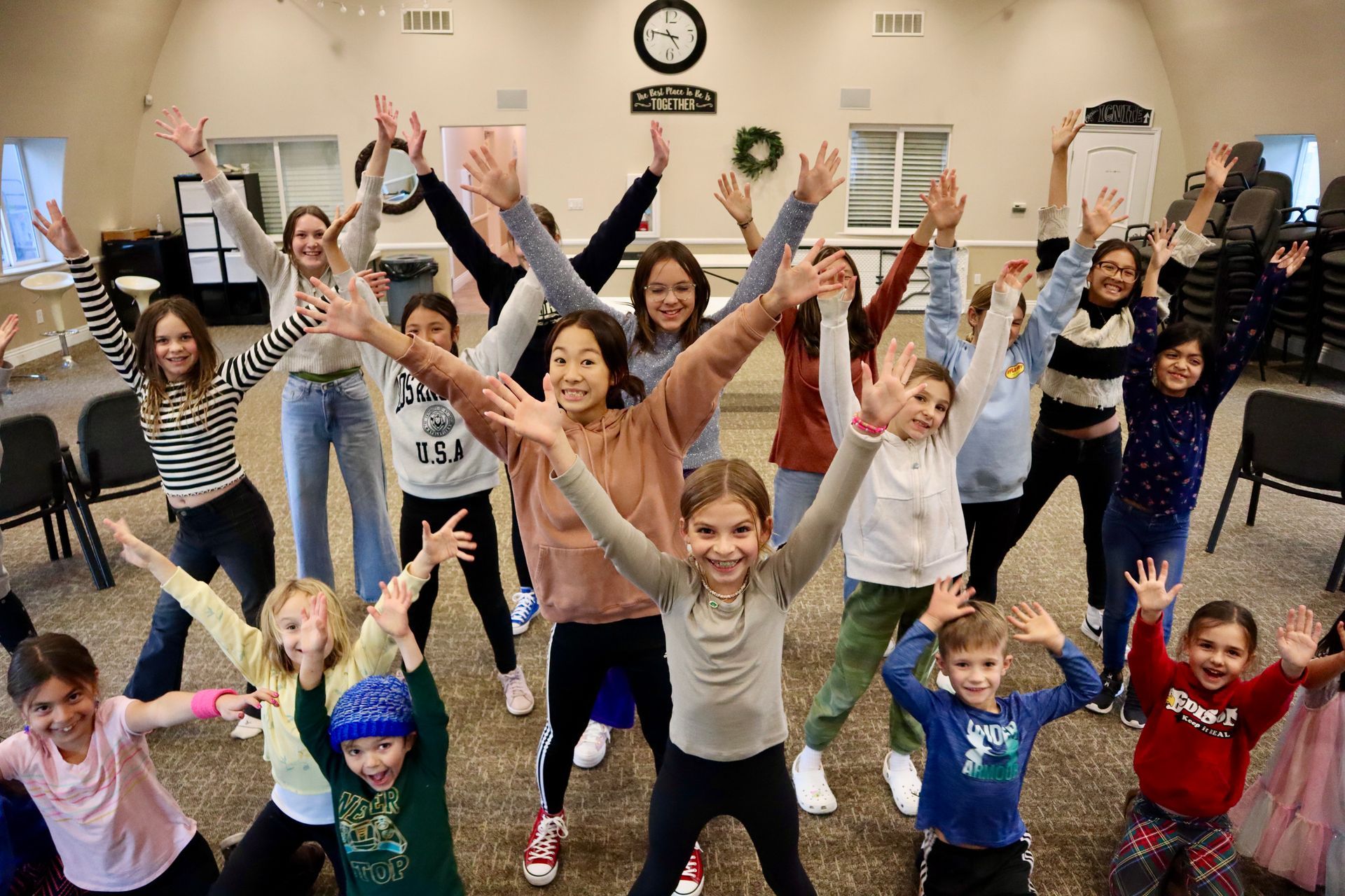 A group of children are standing in a room with their arms in the air.