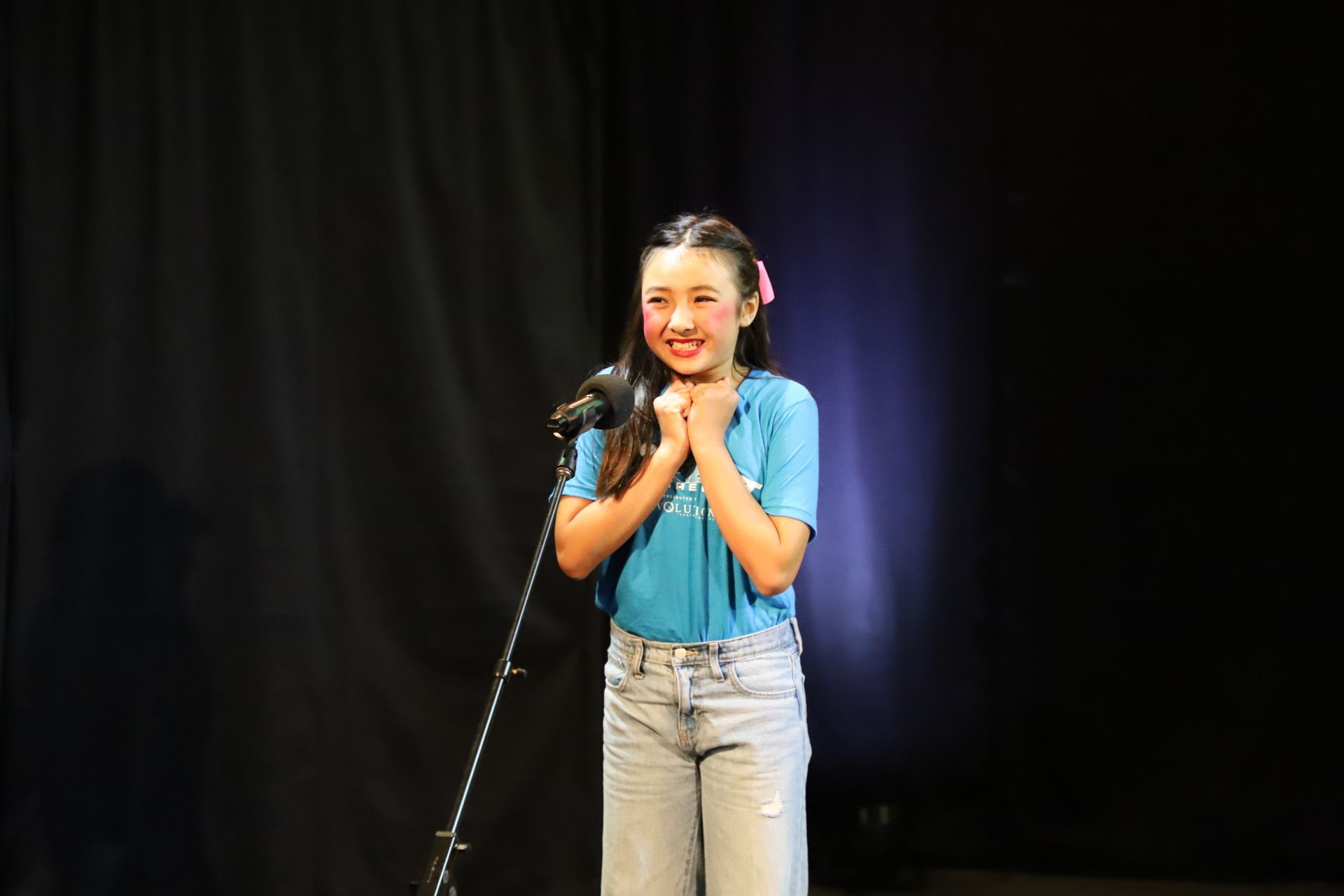 A young girl is standing in front of a microphone on a stage.