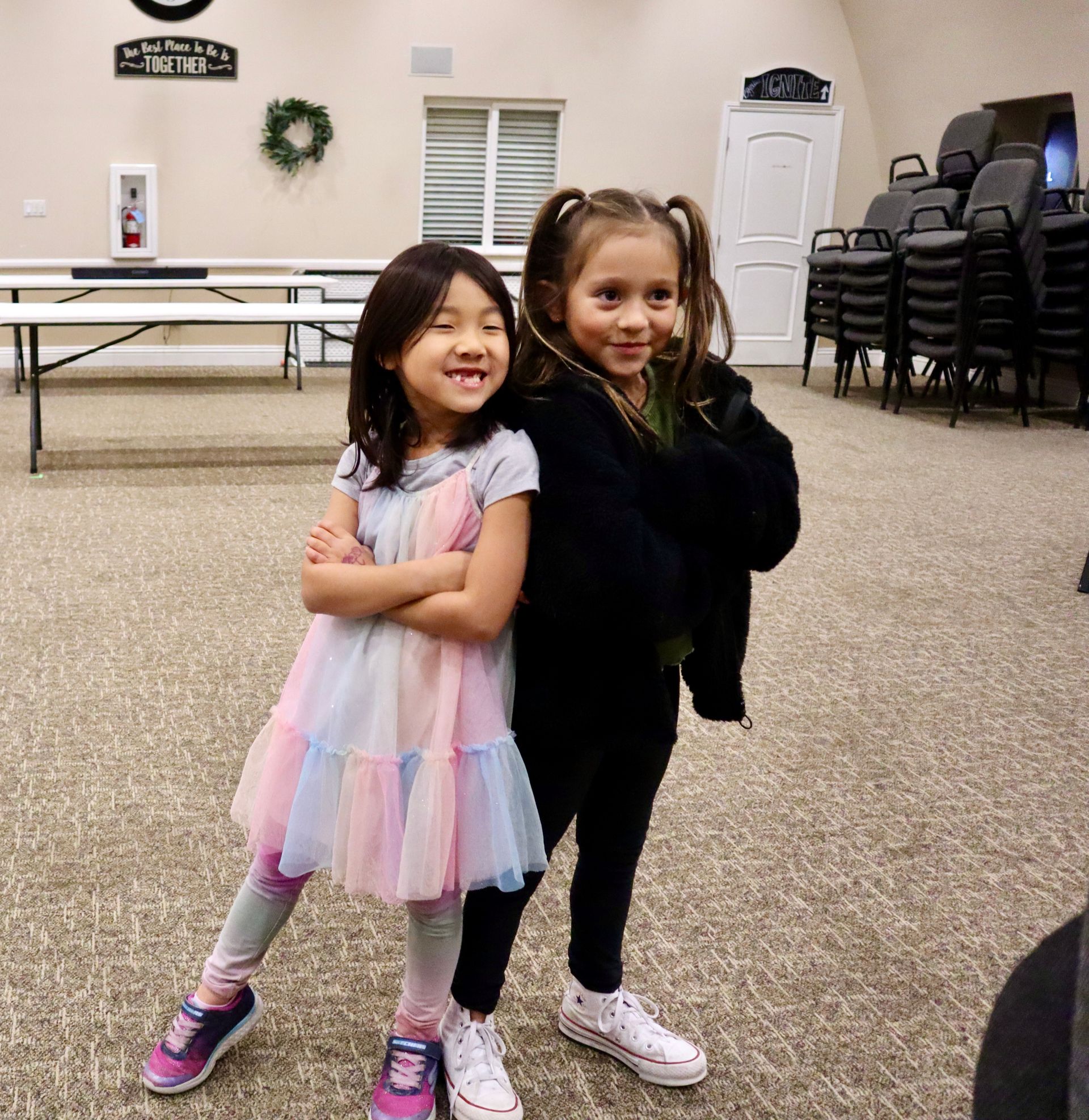 Two little girls standing next to each other in a room with a sign on the wall that says 