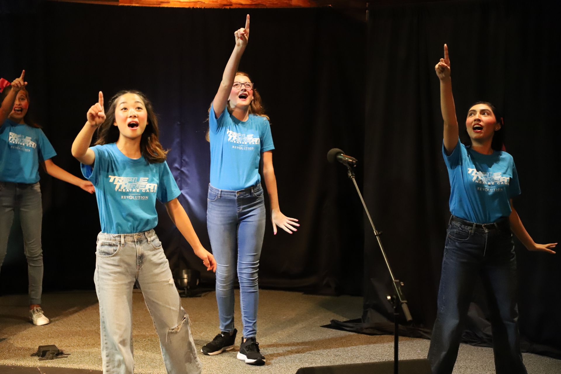 A group of young women are singing into a microphone on a stage.