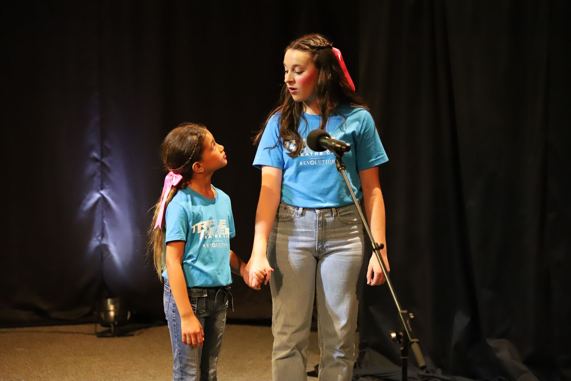 Two young girls are singing into microphones on a stage.