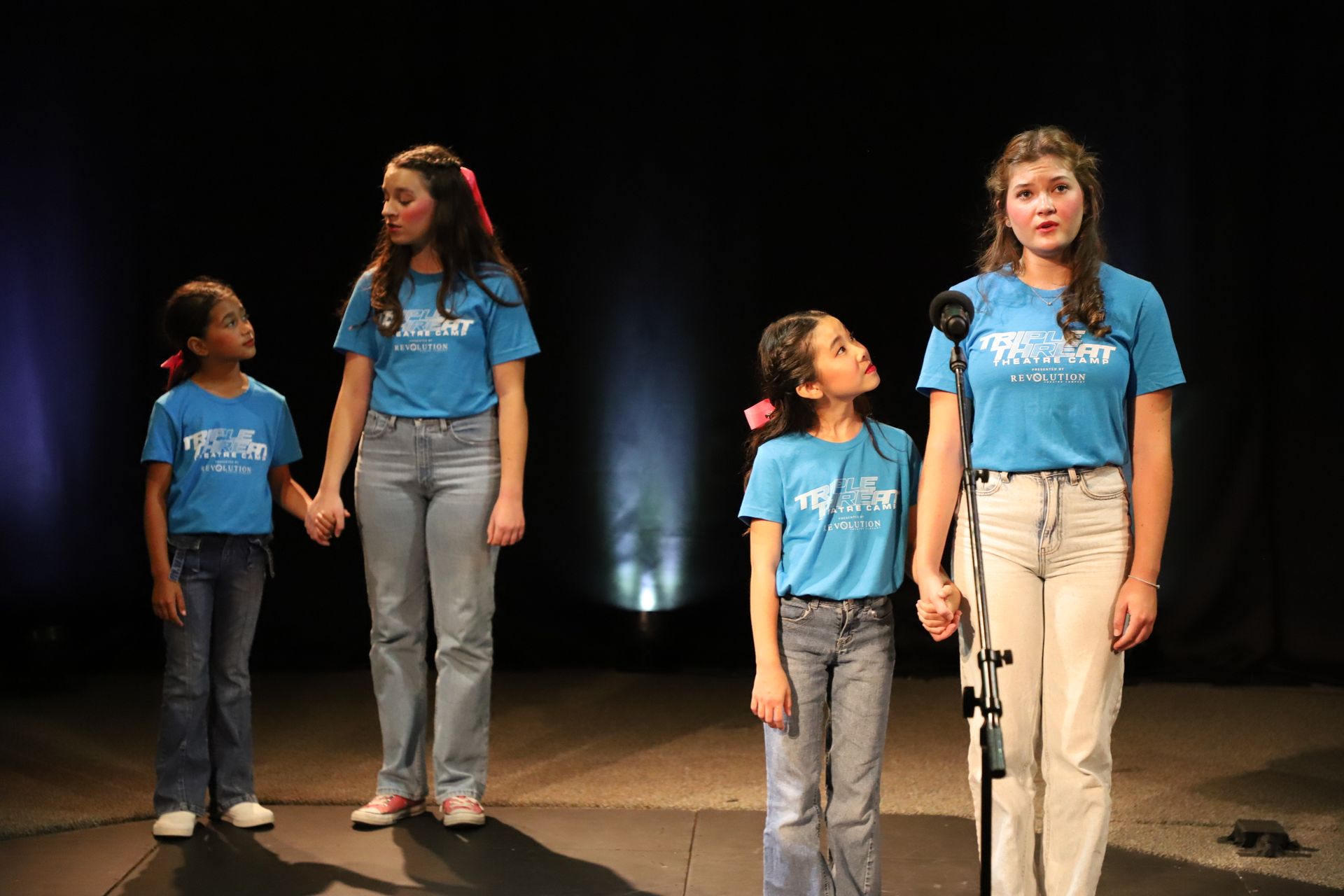 A group of young girls are singing into microphones on a stage.
