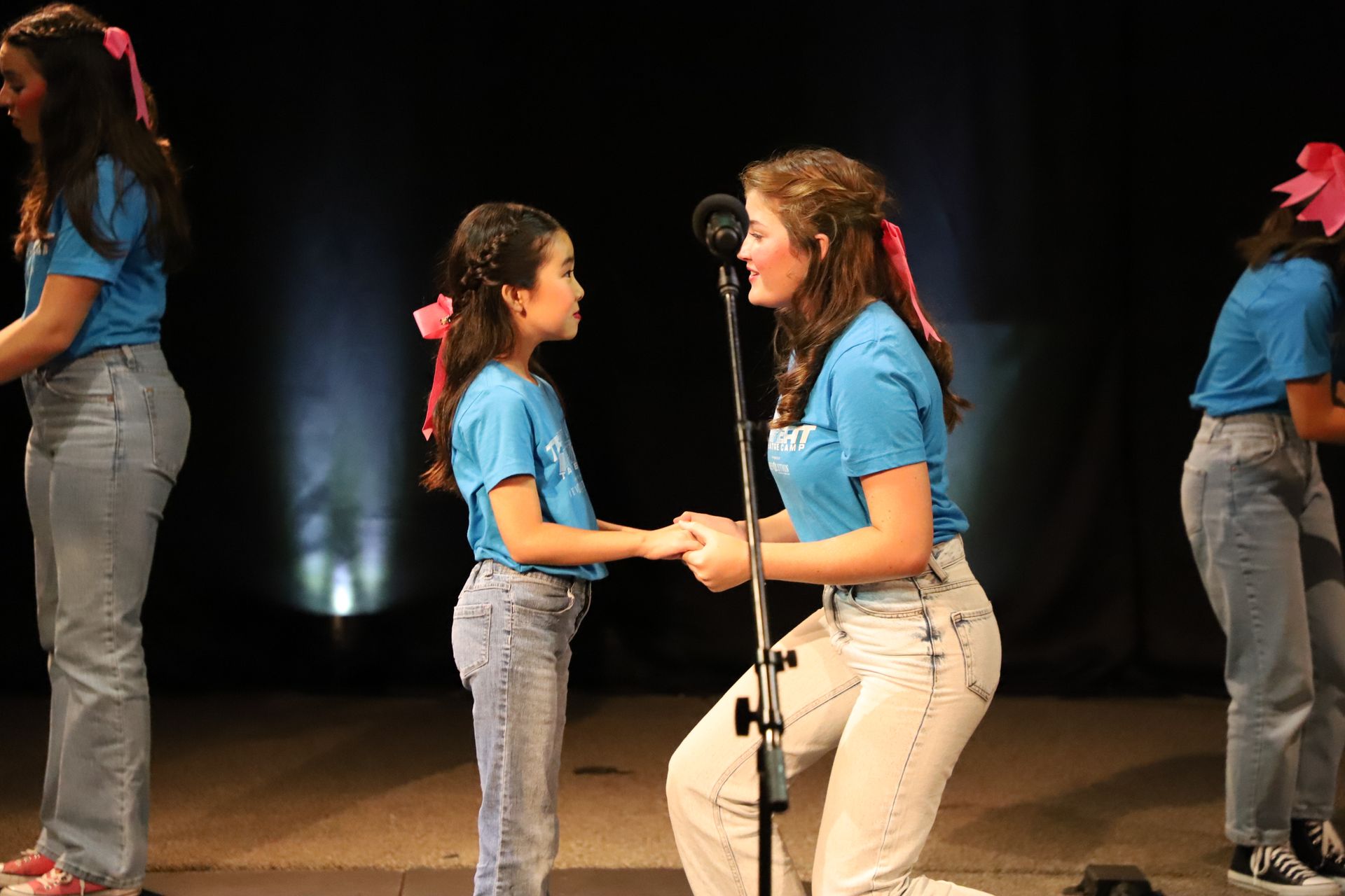 Two girls are holding hands in front of a microphone on a stage.